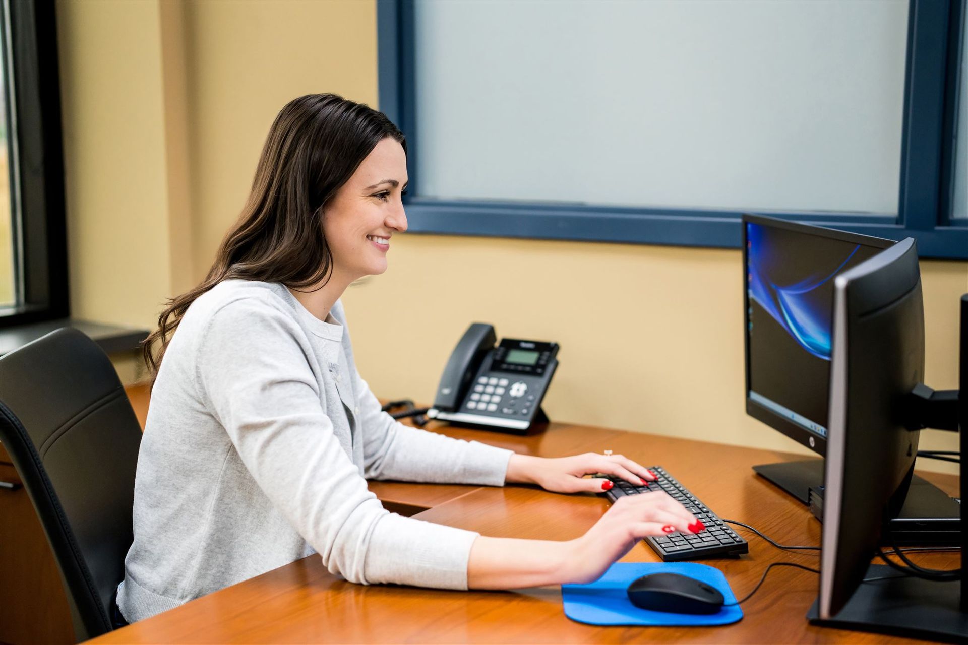 Woman working at a desk with a computer and office phone in an office cubicle