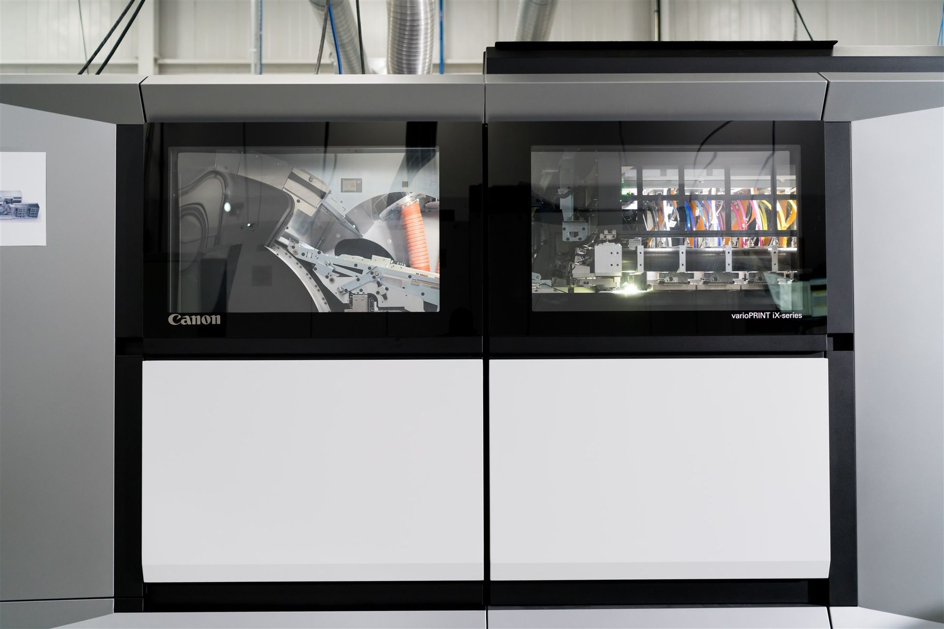 Industrial machine with two black viewing windows and white lower panels in a factory setting