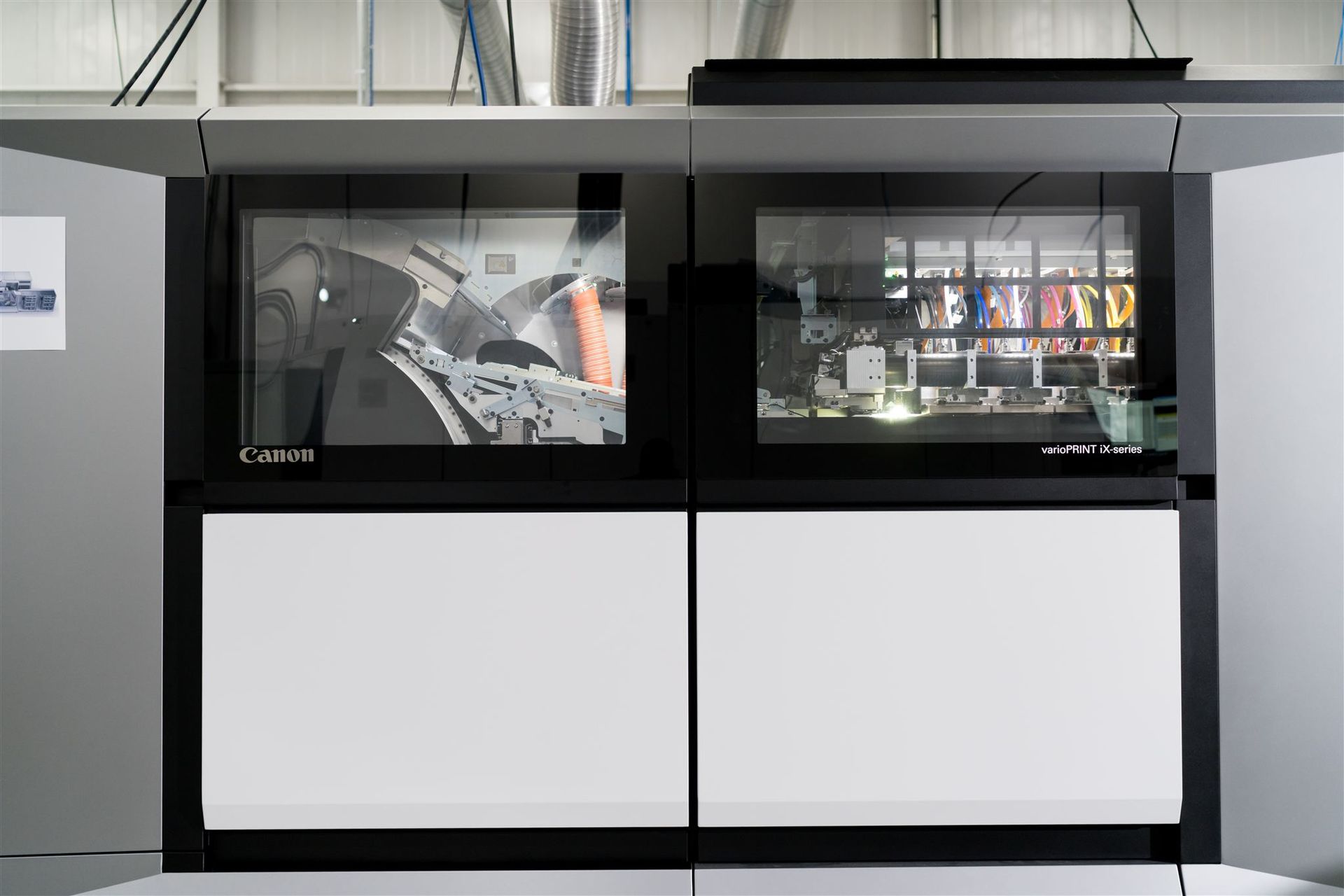 Large industrial machine with two glass-front viewing windows above white lower panels in a factory setting