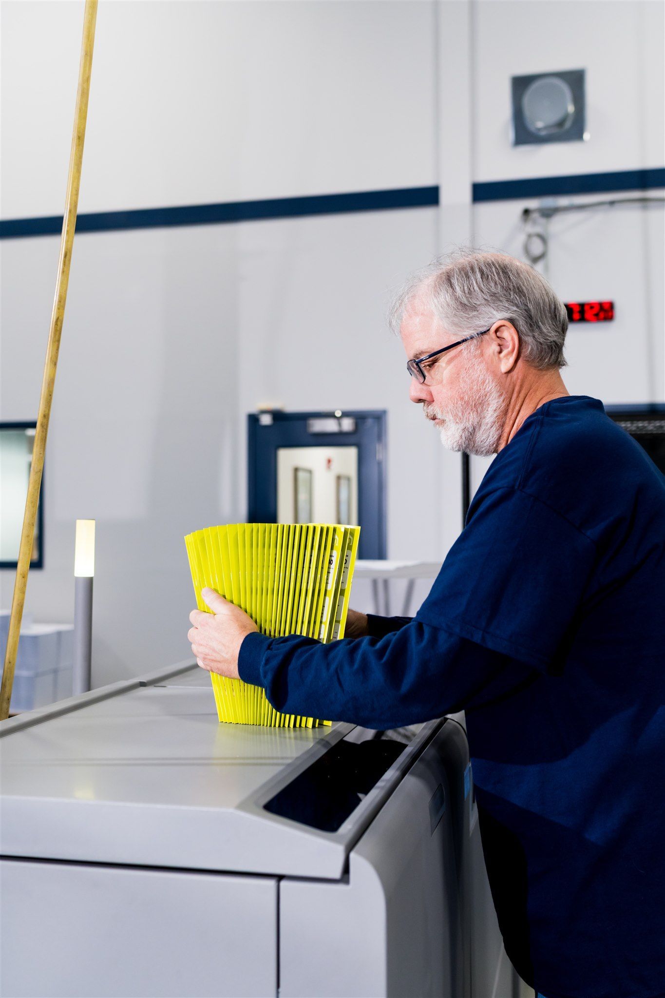 Man in a workshop placing bright yellow parts into a bin beside a machine