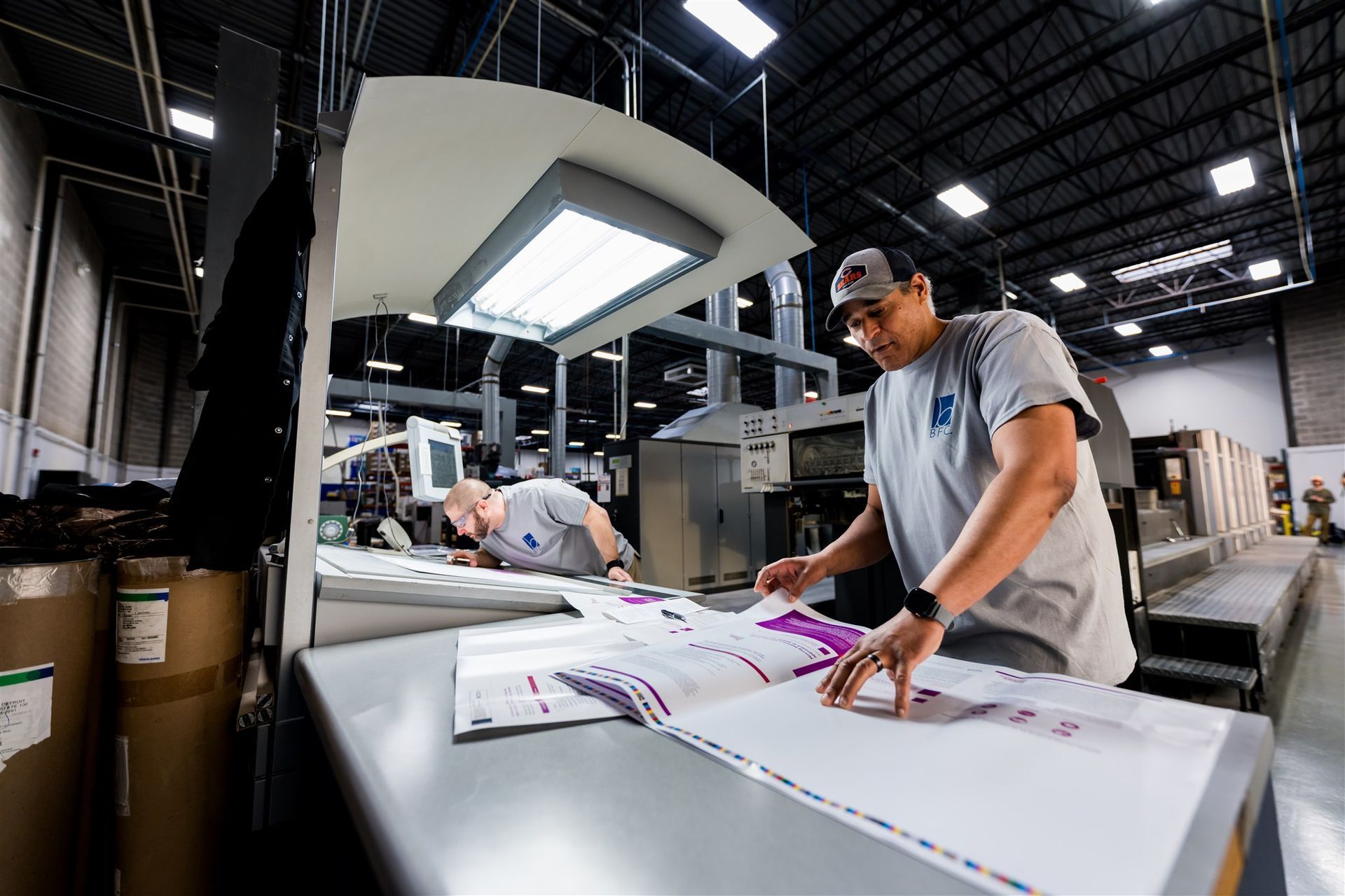 Worker measuring a large printed sheet on a factory press in a print shop