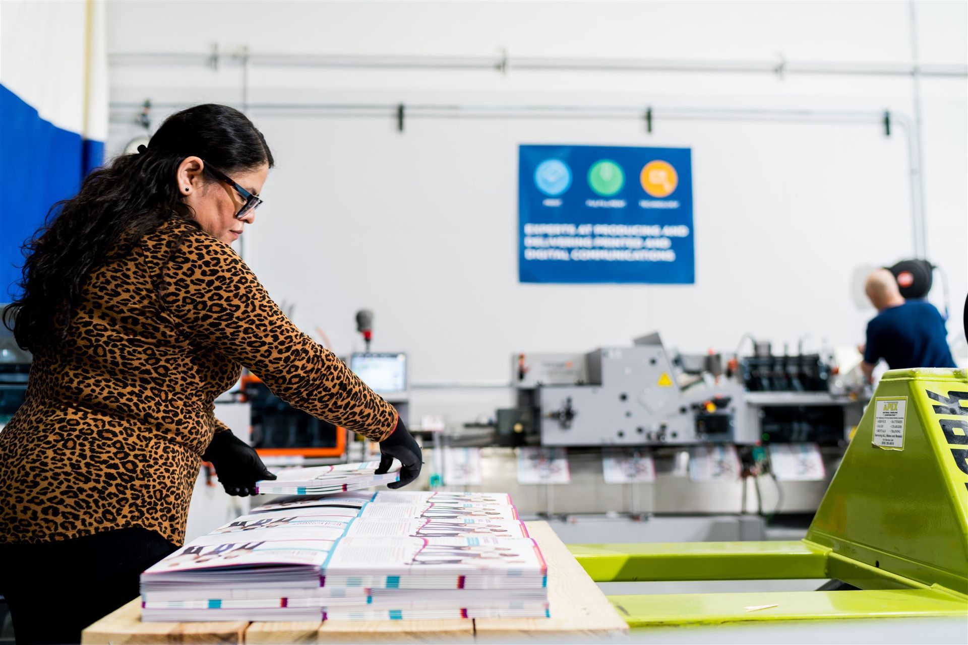 Person sorting stacks of booklets on a table in a bright print shop or warehouse