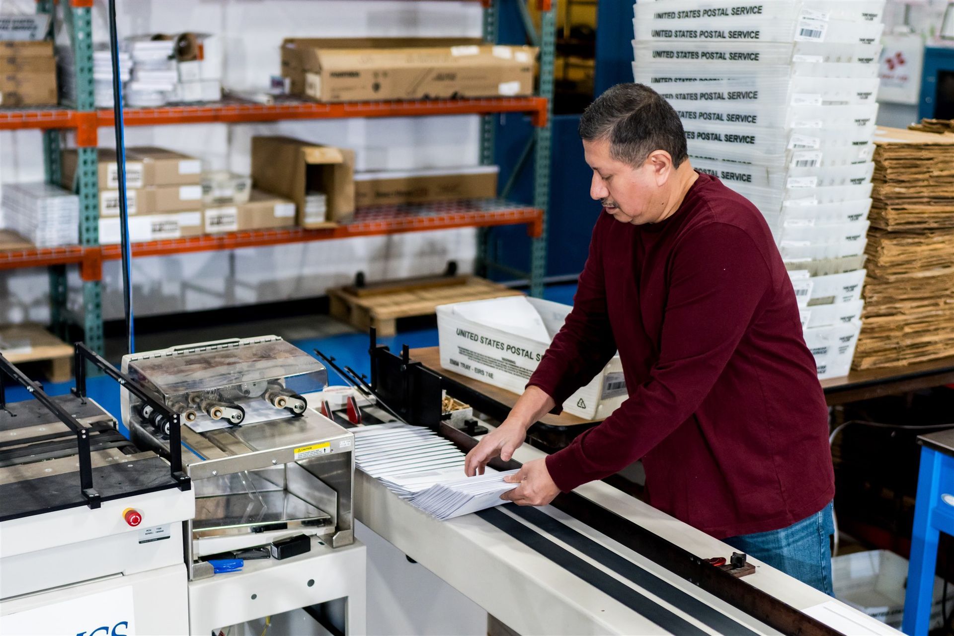 Worker in a warehouse packing items at a conveyor belt with shelves of boxes behind him