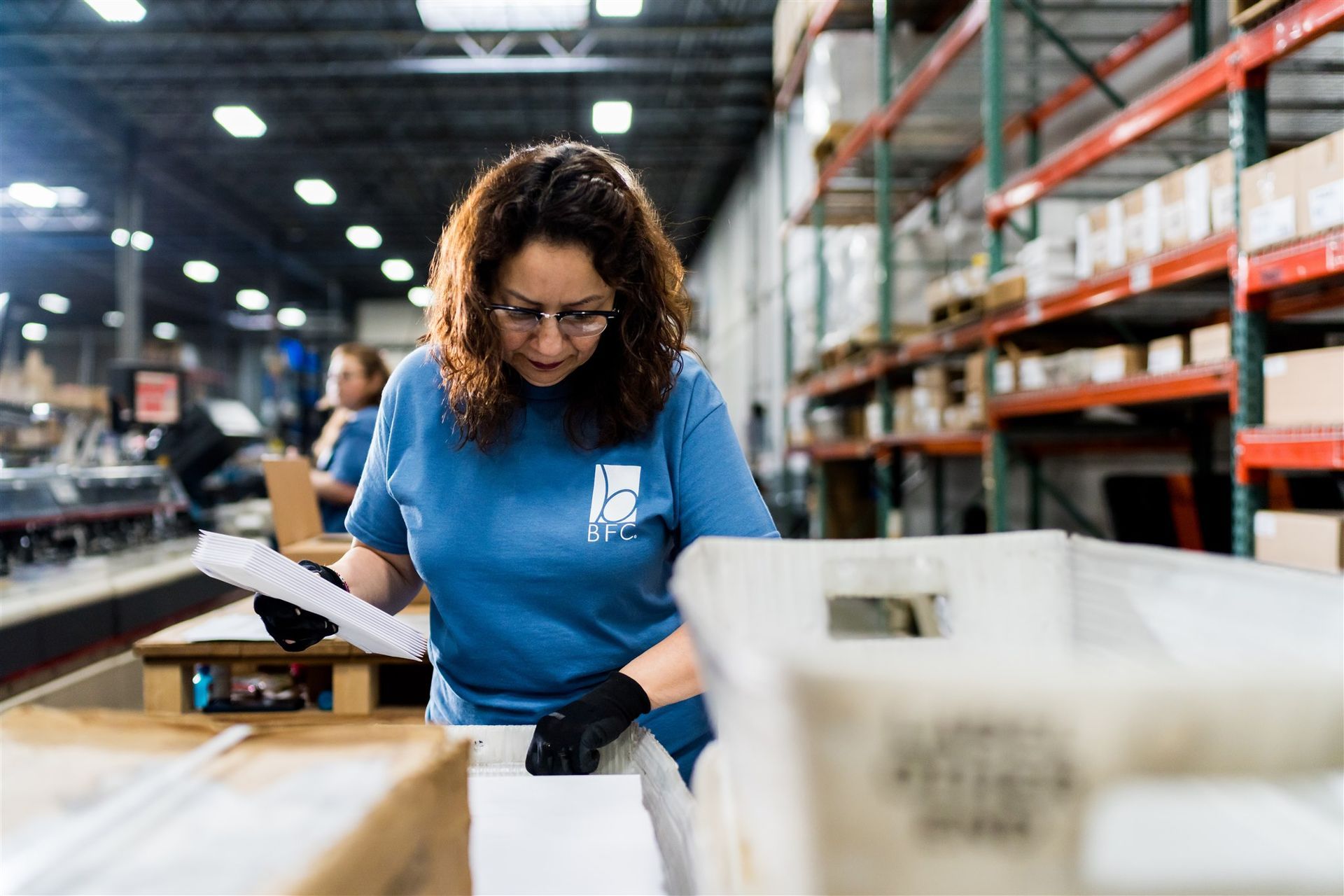 Worker in blue shirt checking inventory in a warehouse aisle with shelves and storage bins