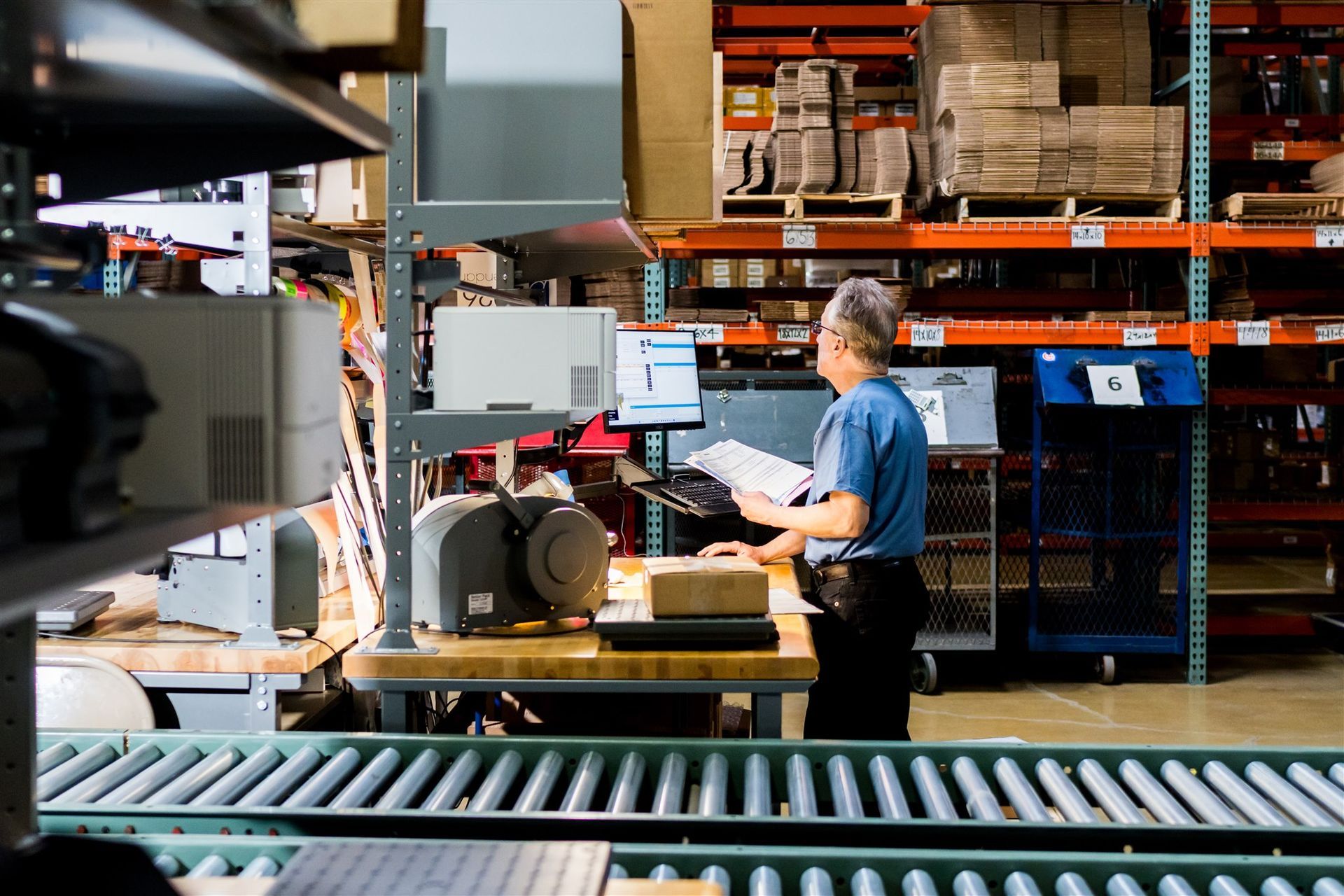 Worker standing at a warehouse machine beside conveyor belts and stacked pallets
