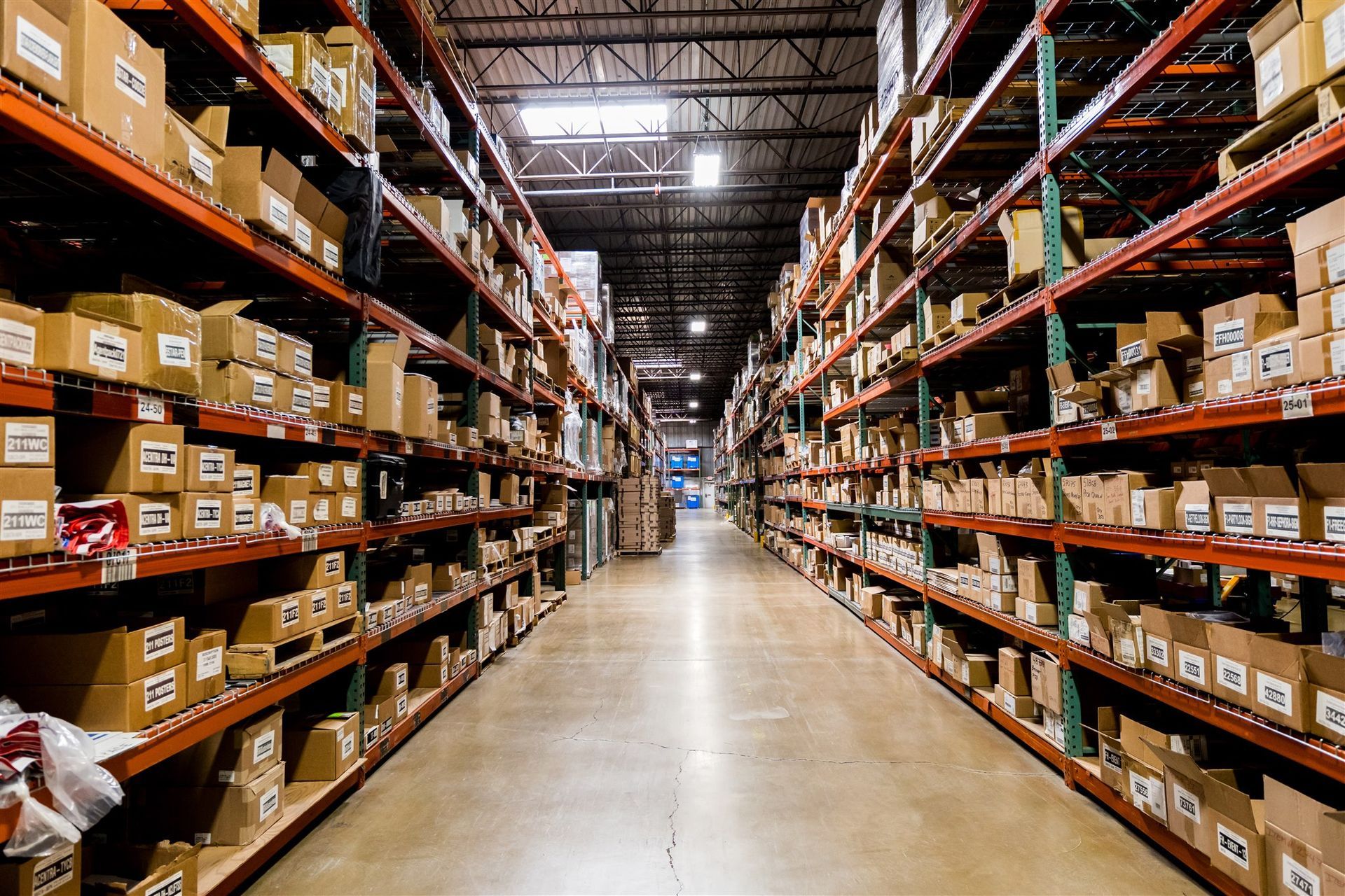 Aisle in a warehouse with tall shelves stocked with boxes and supplies on both sides