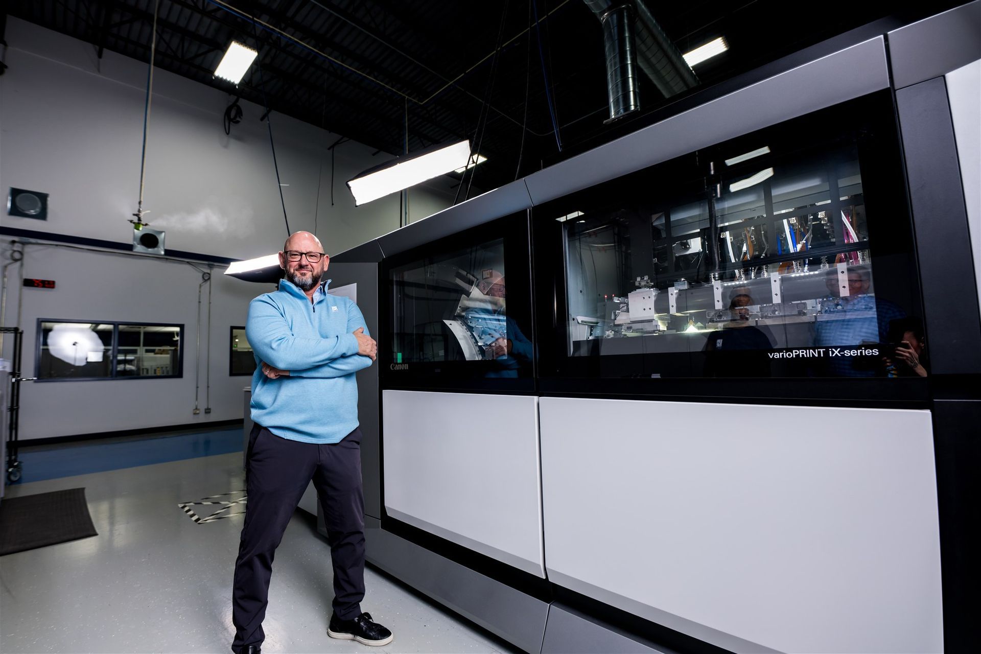 Man standing in a lab beside large industrial equipment and a viewing window.