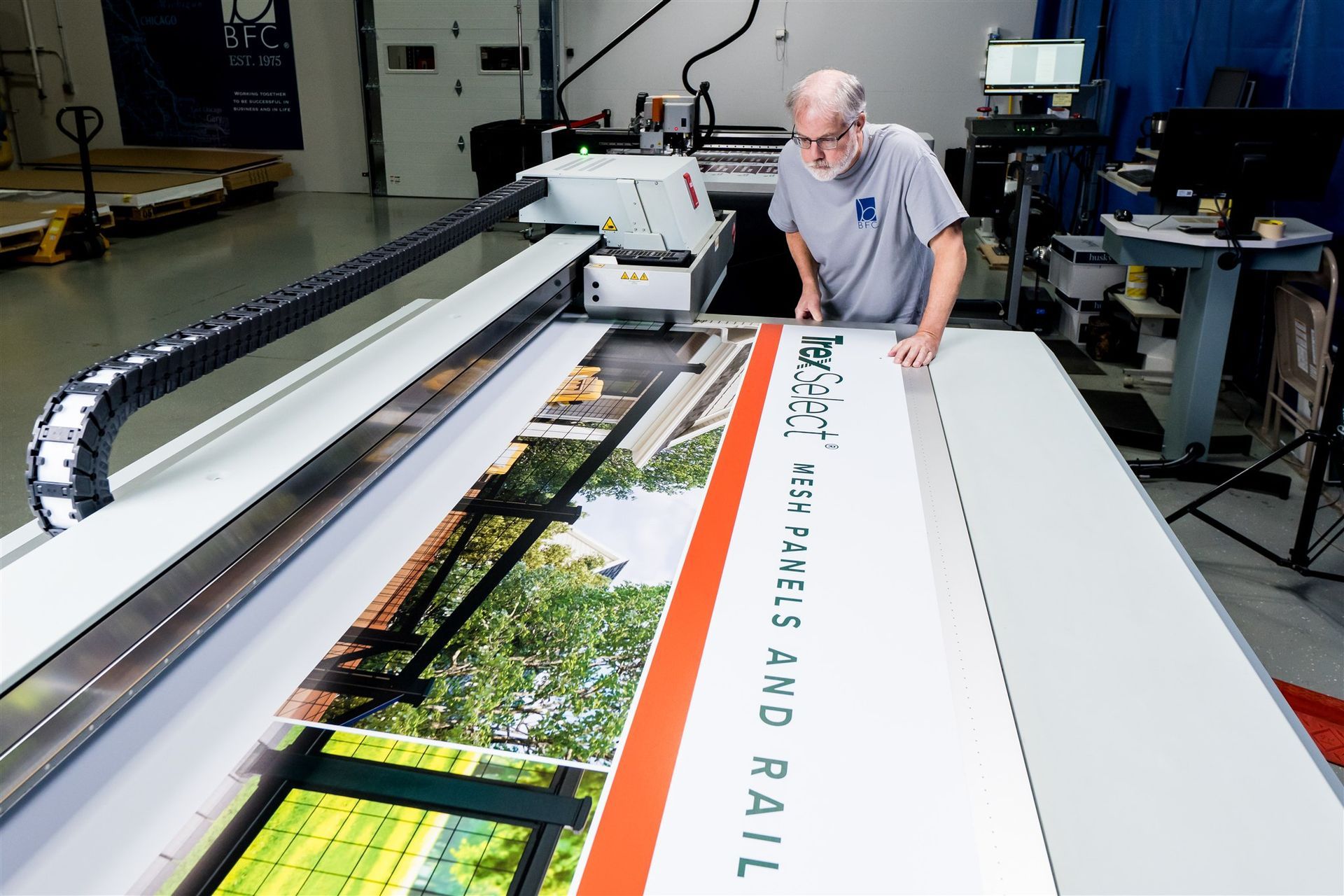 Man operating a large-format printer producing a colorful banner in a workshop