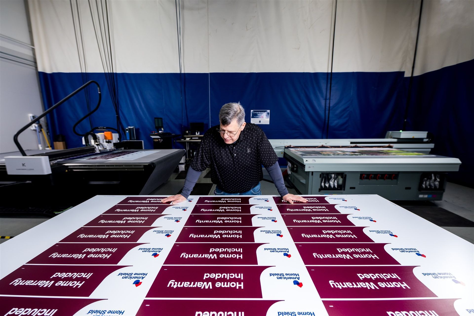 Person arranging maroon-and-white campaign posters on a large table in a print shop
