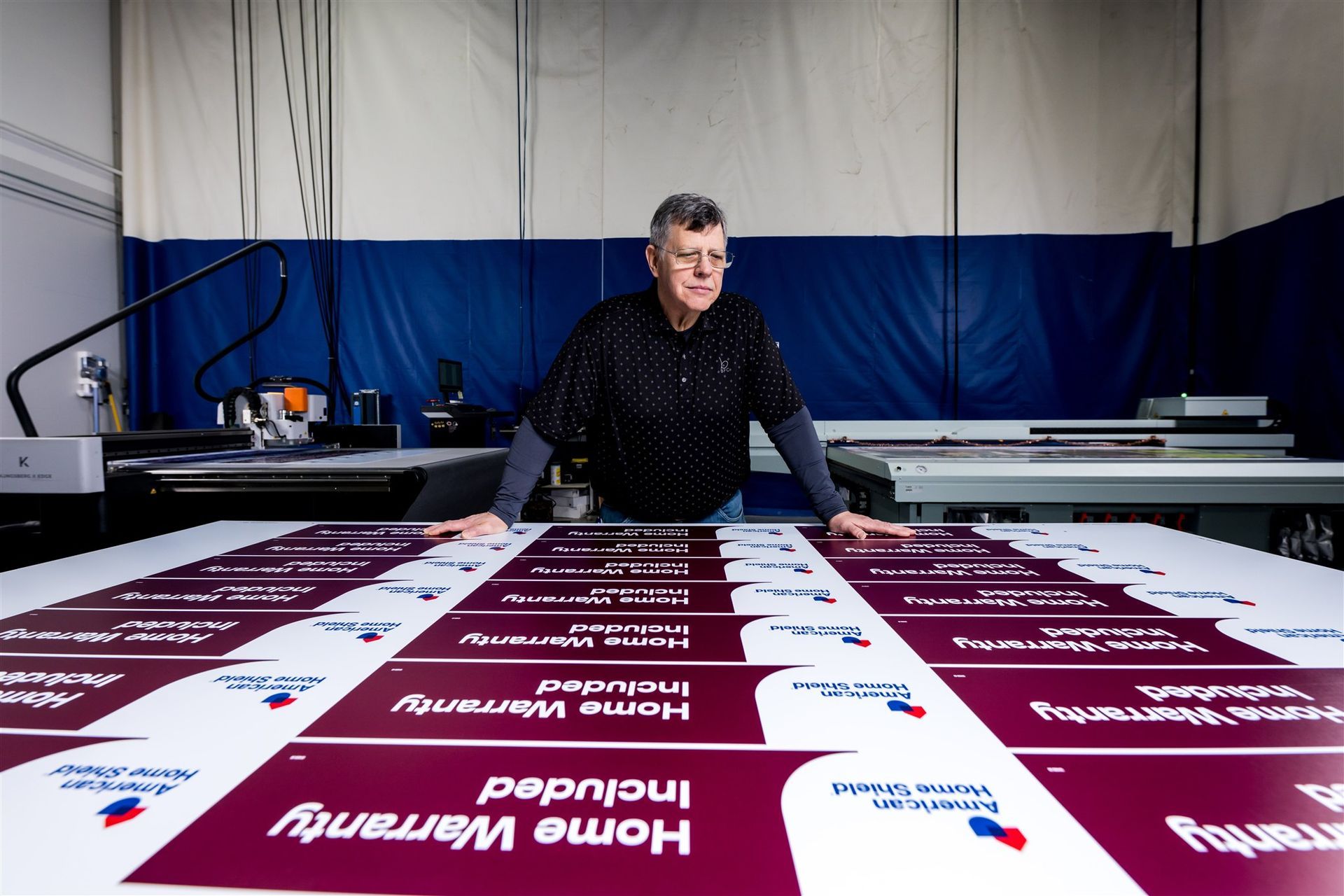 Person in a workshop holding a large printed banner with maroon labels laid out on a table