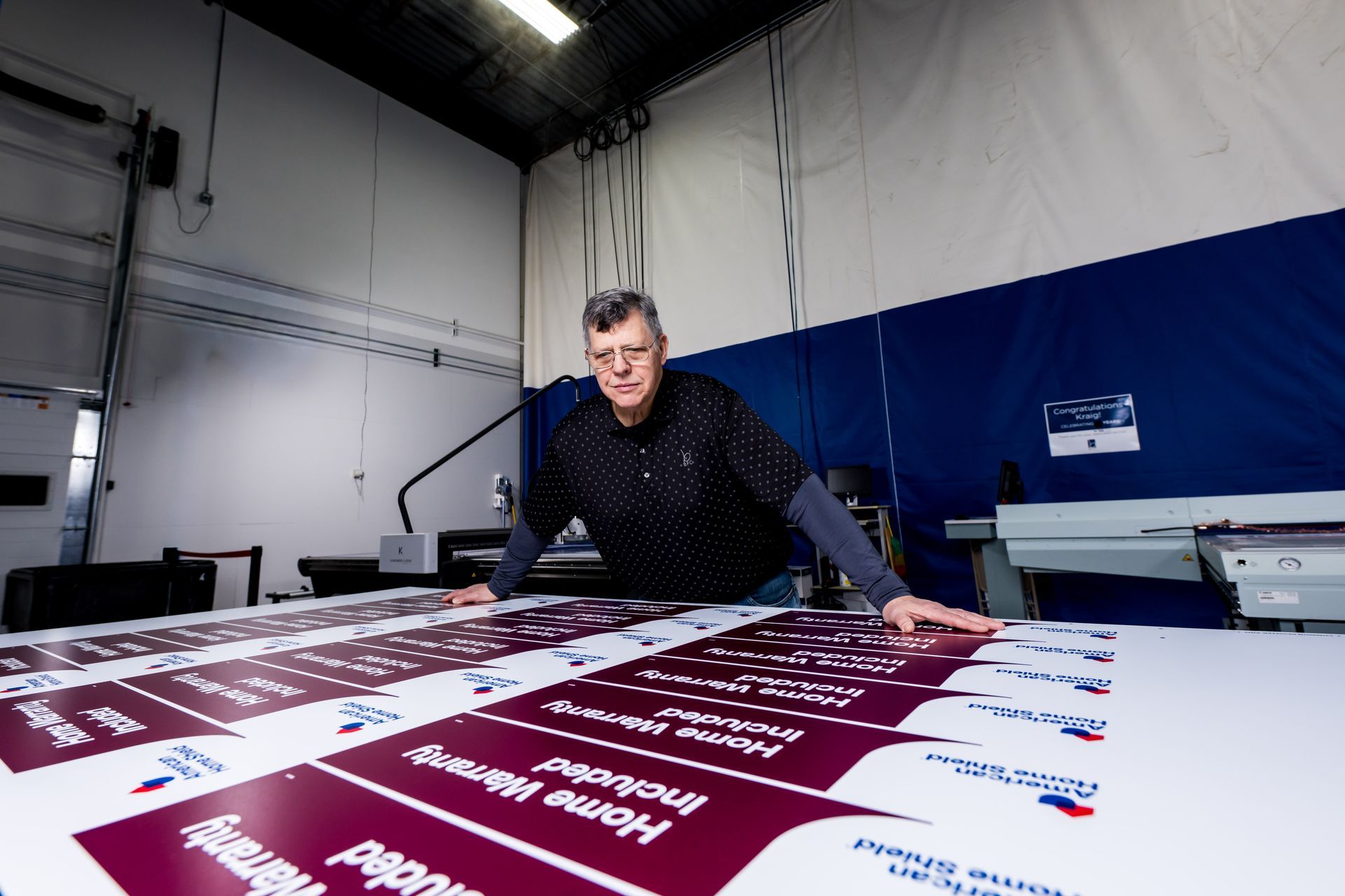 Man in a workshop leaning over large printed maroon and white sheets on a table