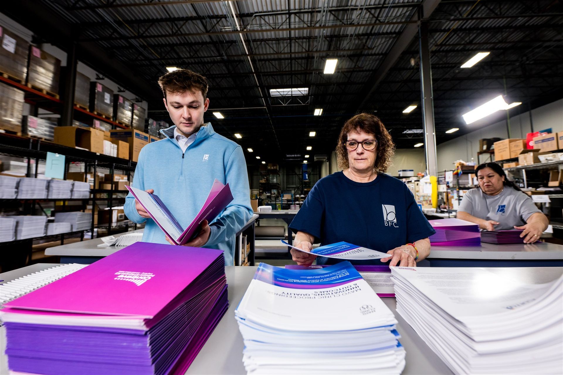 Workers sorting stacks of papers in a warehouse, with bright pink and white piles in the foreground