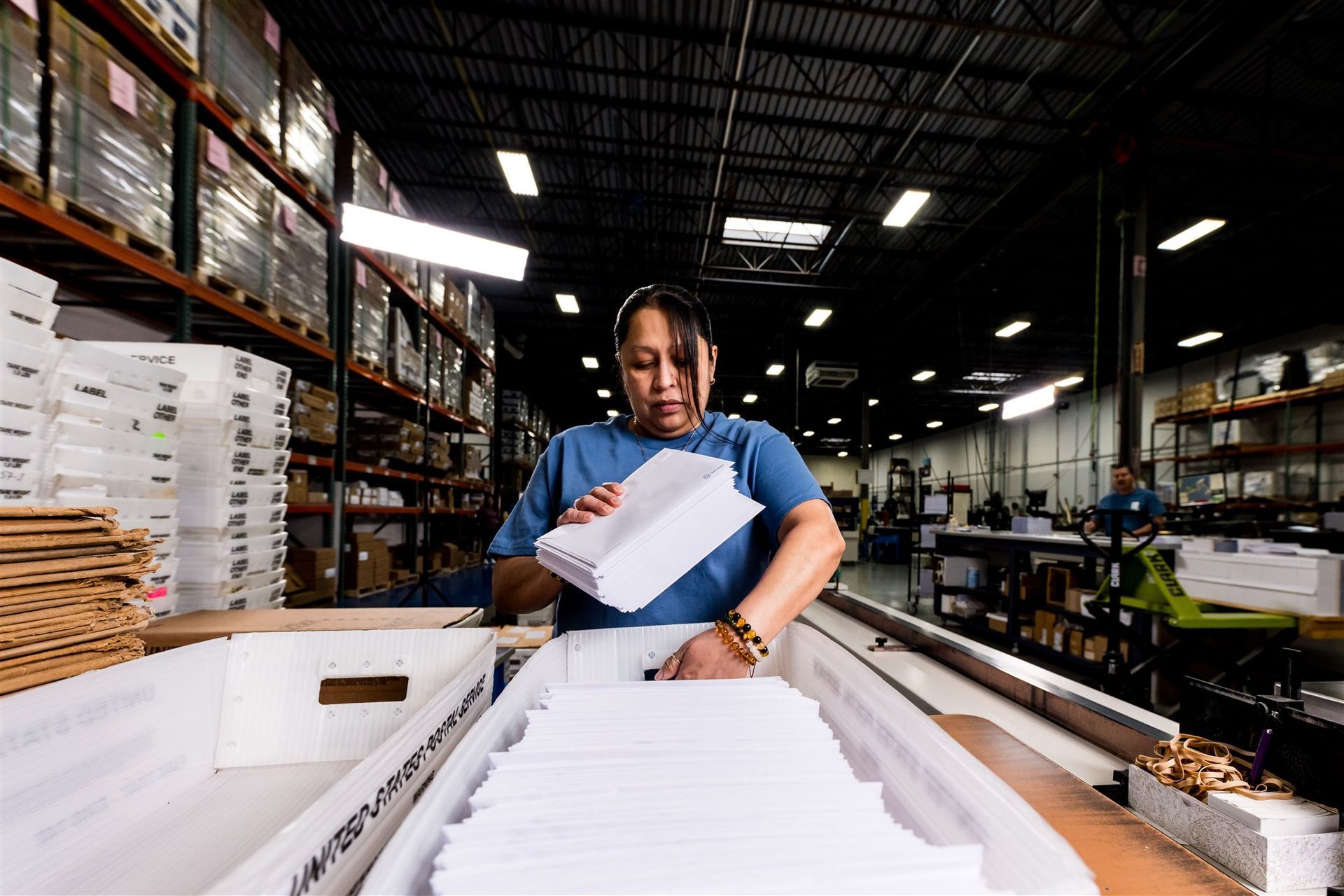 Worker sorting stacks of white paper on a conveyor in a warehouse
