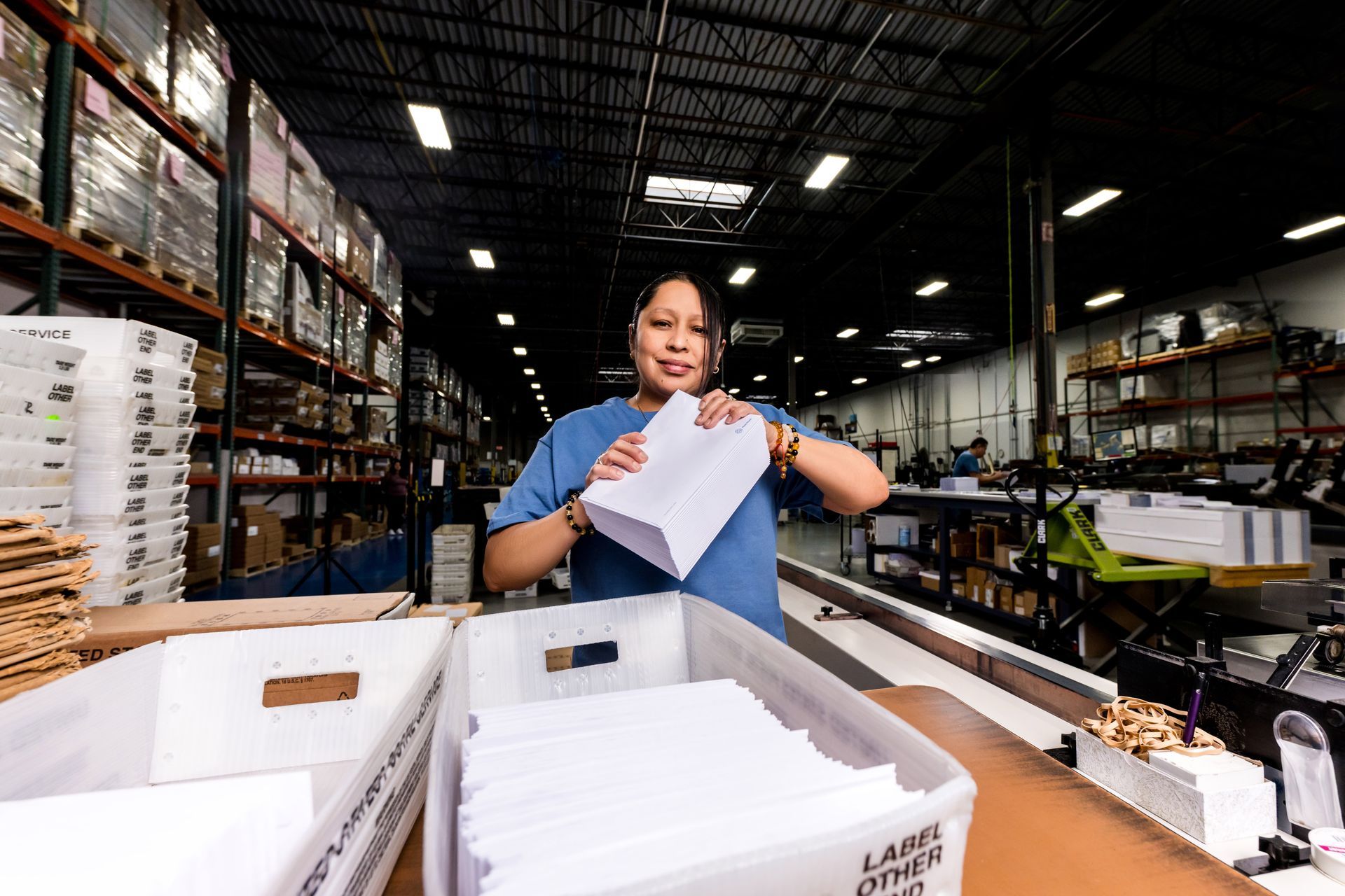 Worker sorting papers in a warehouse aisle with shelves and boxes around her