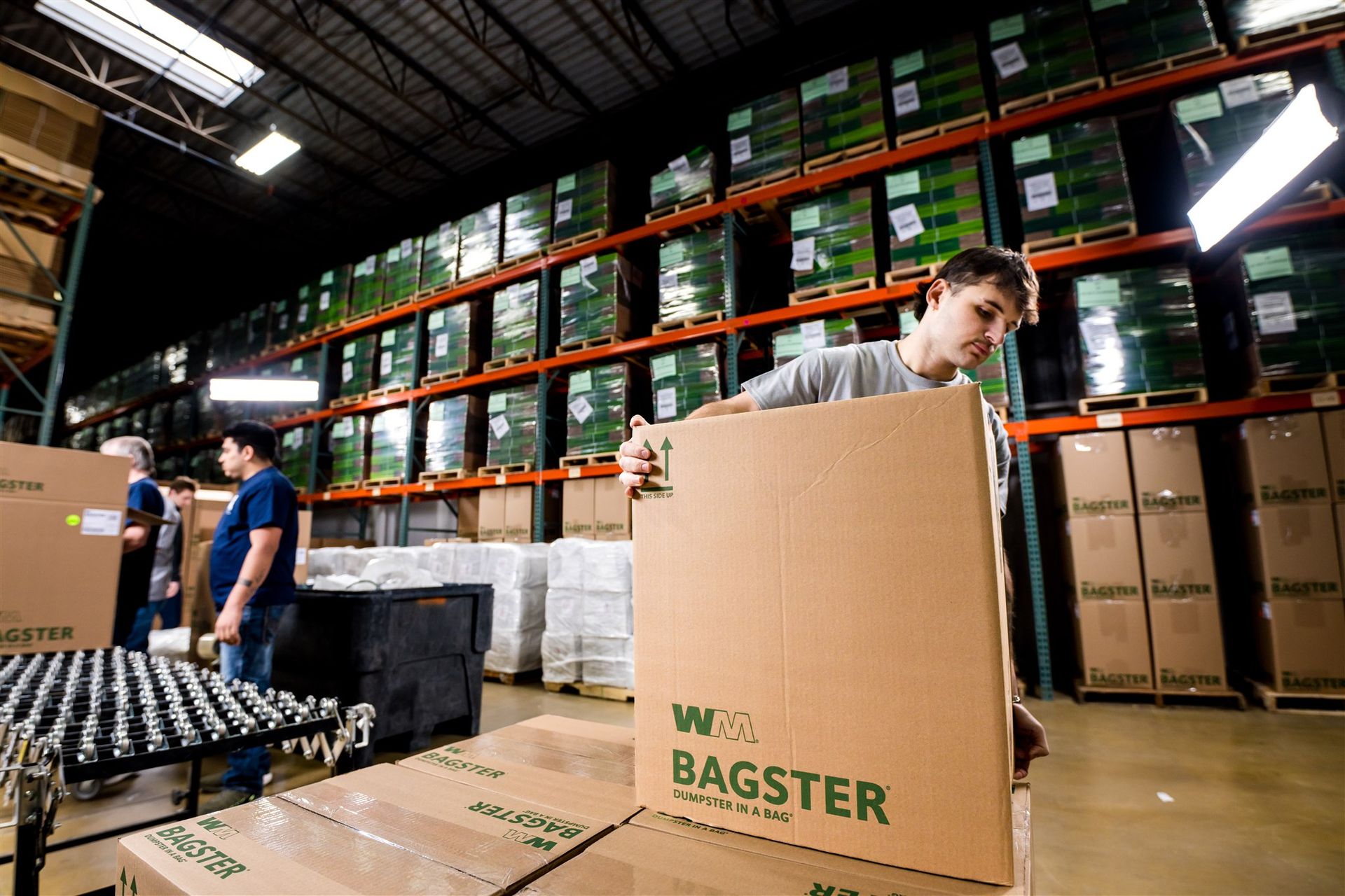 Workers packing boxes in a warehouse with stacked pallets and shelves of goods