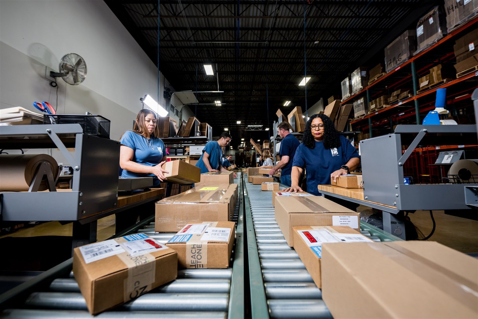 Workers packing cardboard boxes on a warehouse conveyor belt with moving parcels