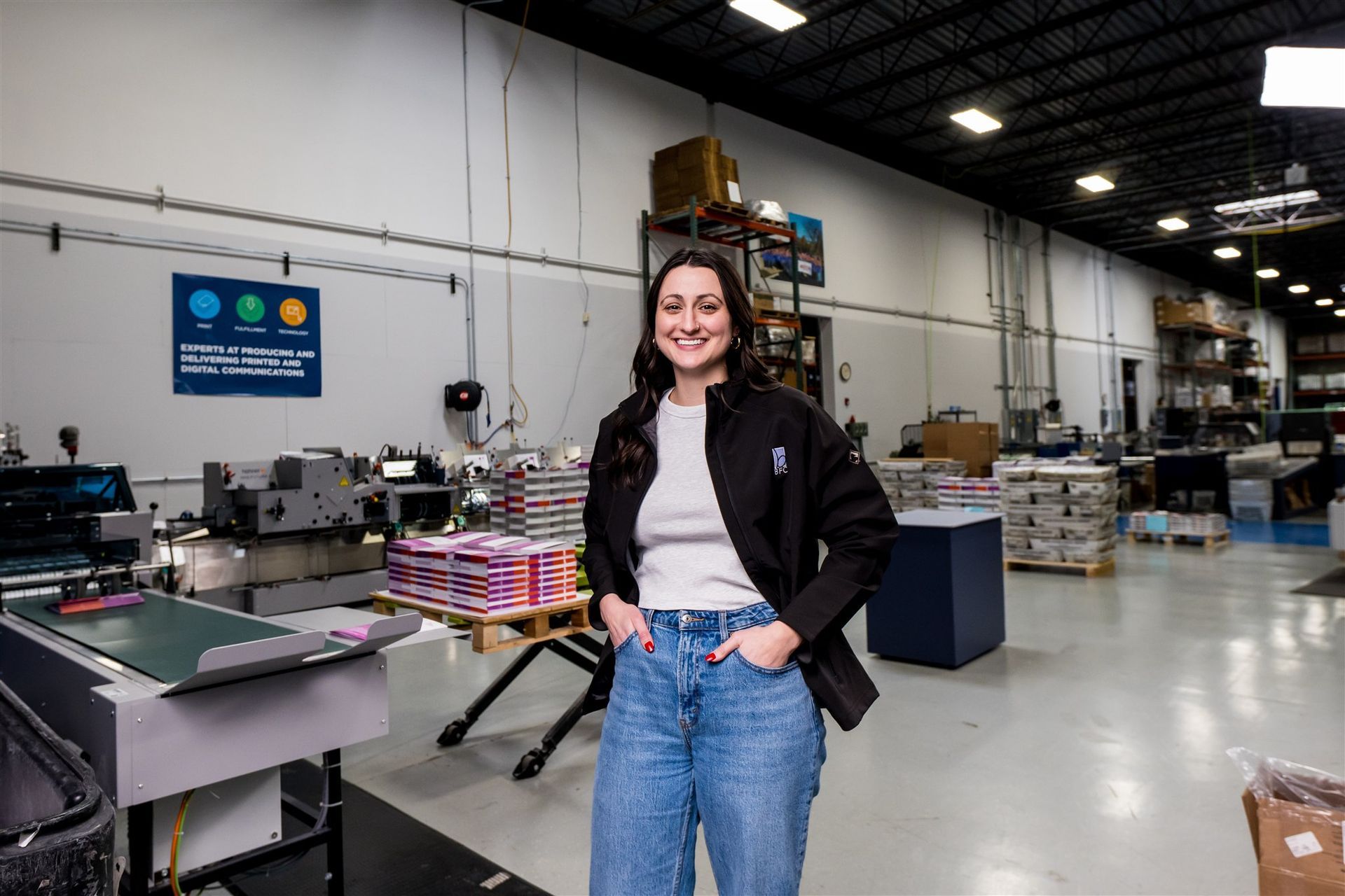 Woman standing in a warehouse workshop beside equipment and stacked materials