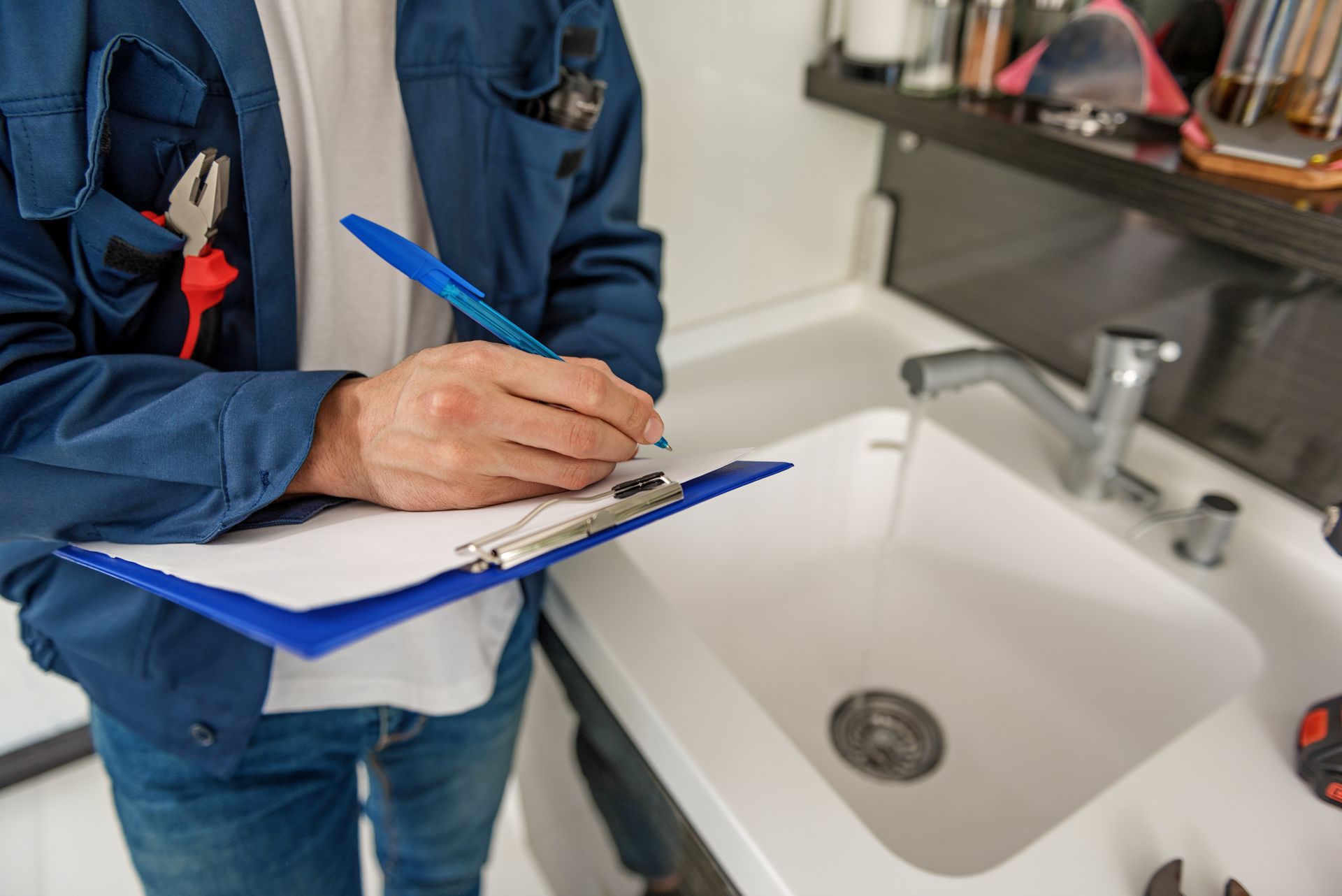 A plumber is writing on a clipboard in front of a sink.