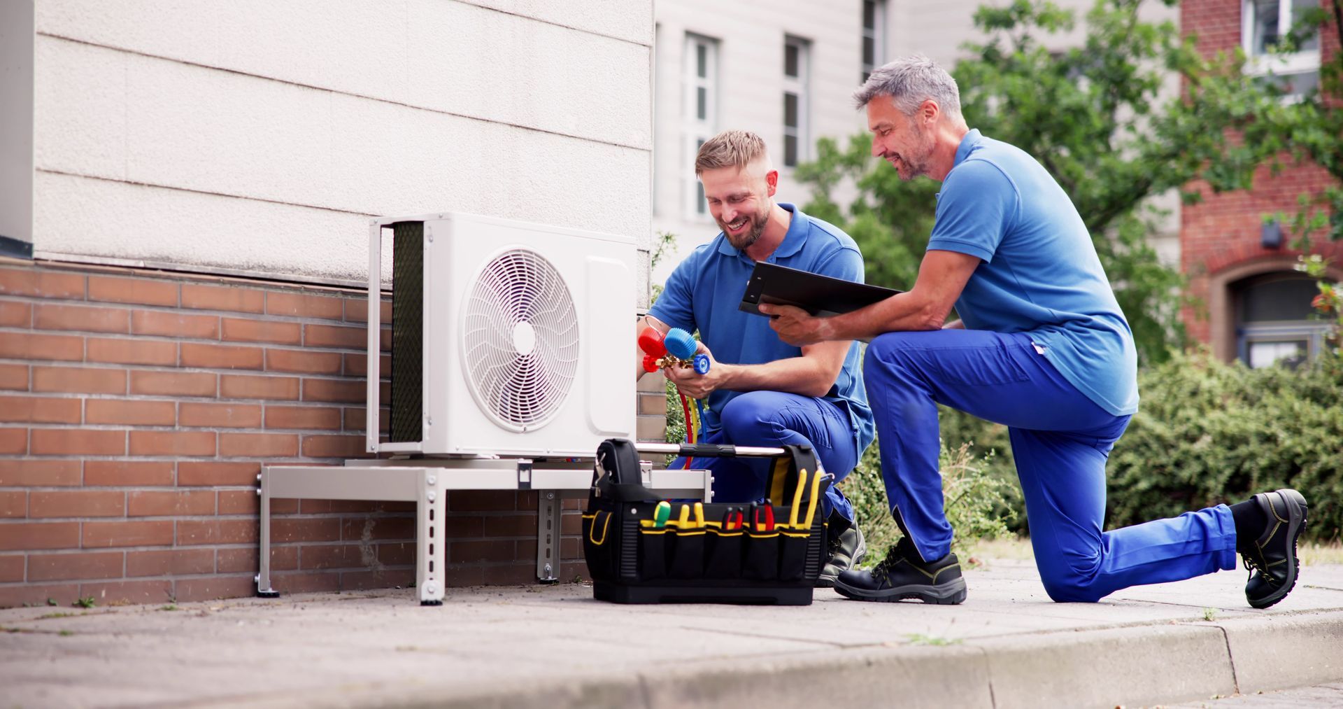 Two HVAC professionals performing maintenance on an exterior air conditioning system.