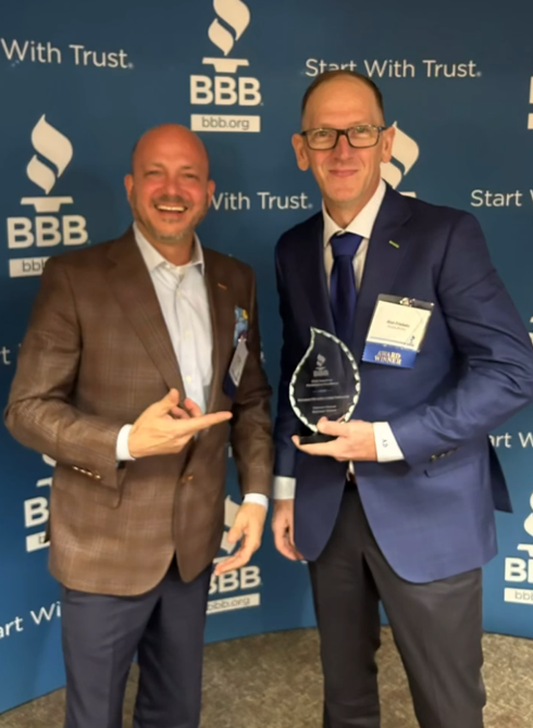 Two men are posing for a picture in front of a banner that says bbb