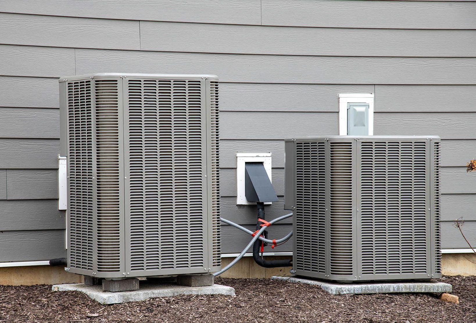 Two air conditioners are sitting on the side of a house.
