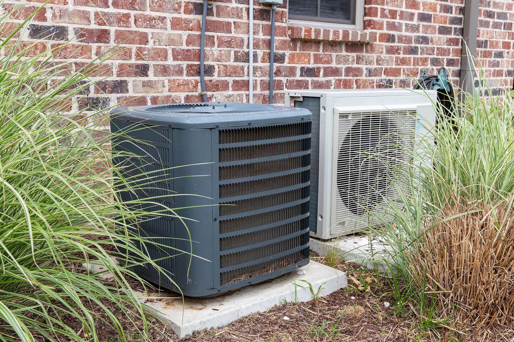 Two air conditioners are sitting on the side of a brick building.