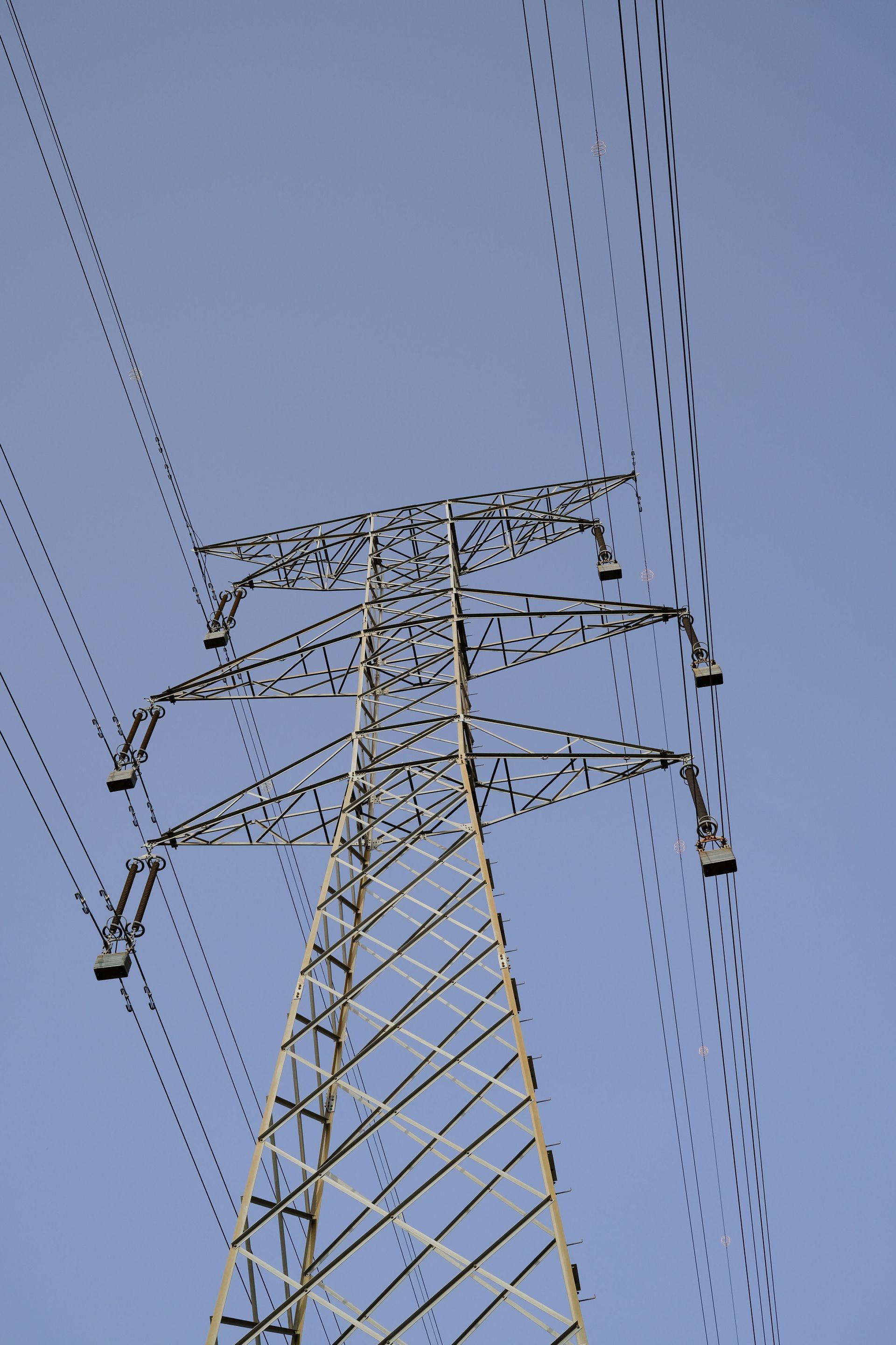Tall electrical transmission tower with power lines against a clear blue sky