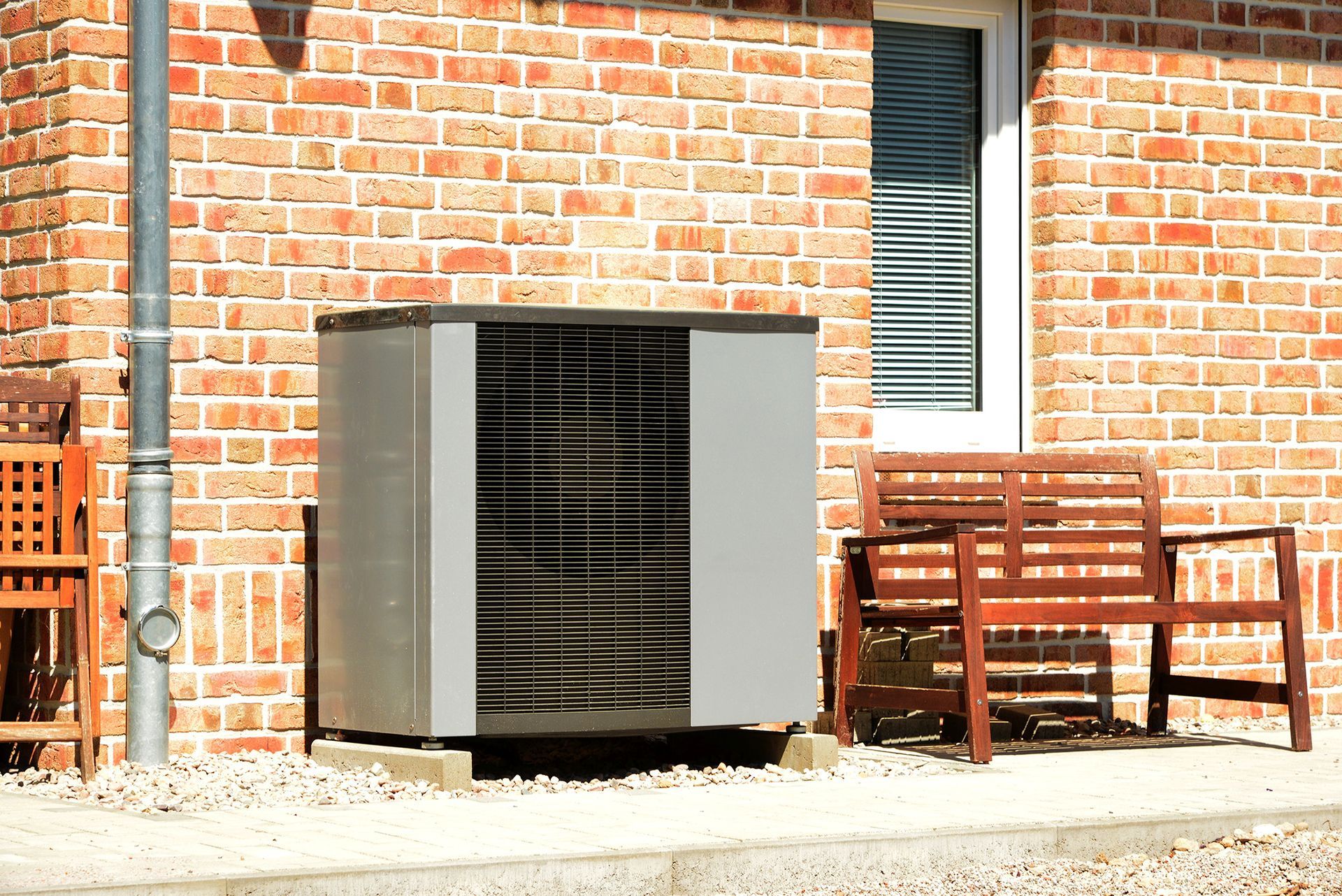 Heat pump unit outside brick house with a bench.