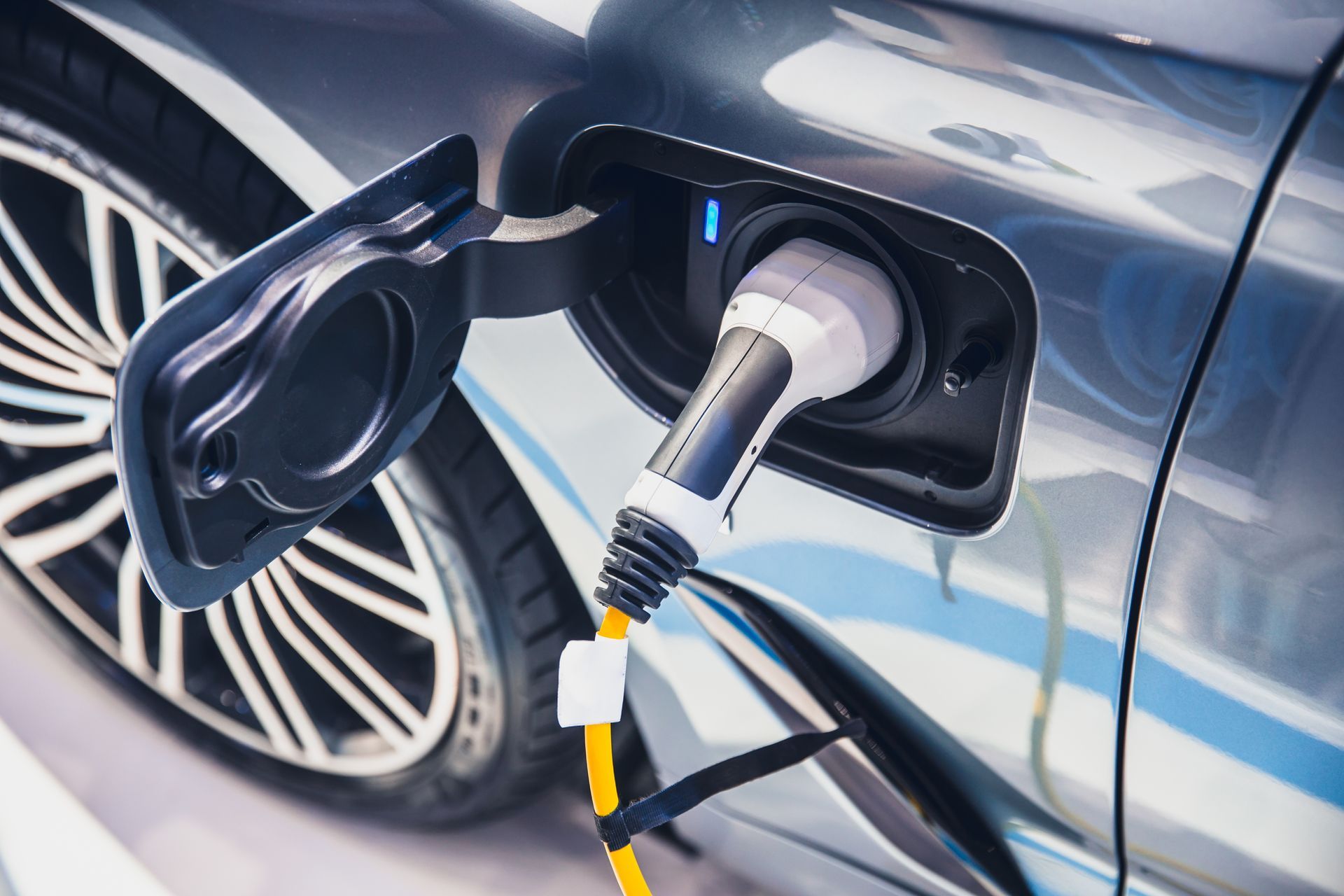 Electric car charging at a public station, with cable plugged into a blue vehicle.