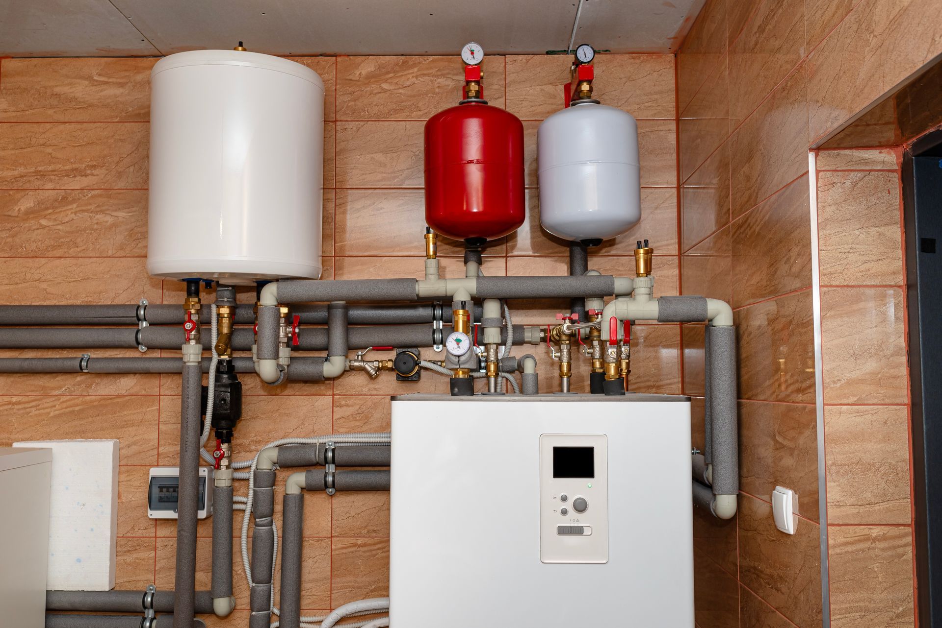 Heating system with white tank, red and white expansion tanks, and insulated pipes.