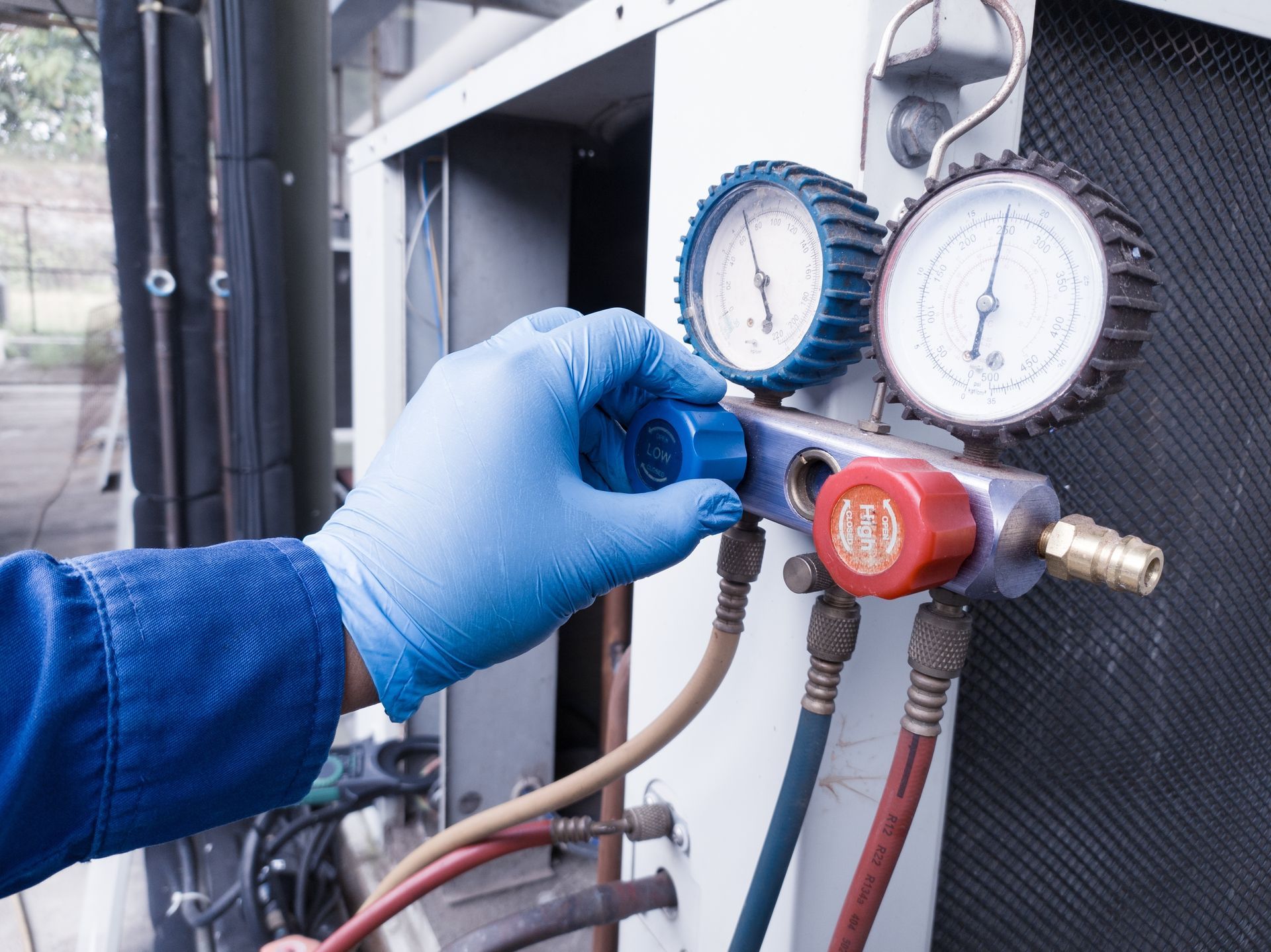 Hand in blue glove turning valve on refrigeration gauges.
