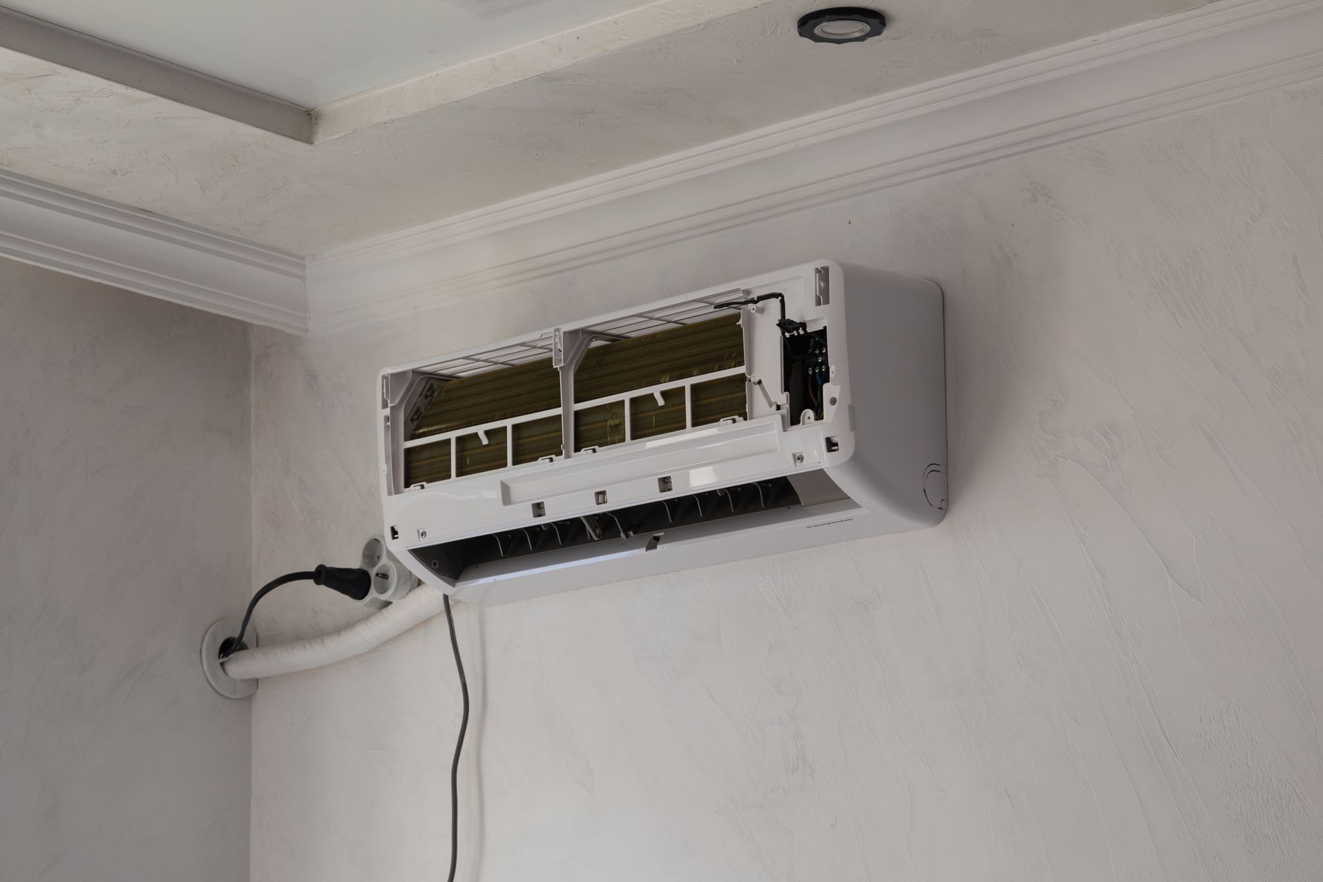 Wall-mounted air conditioner unit with the front cover removed, showing internal components and a hanging cable.