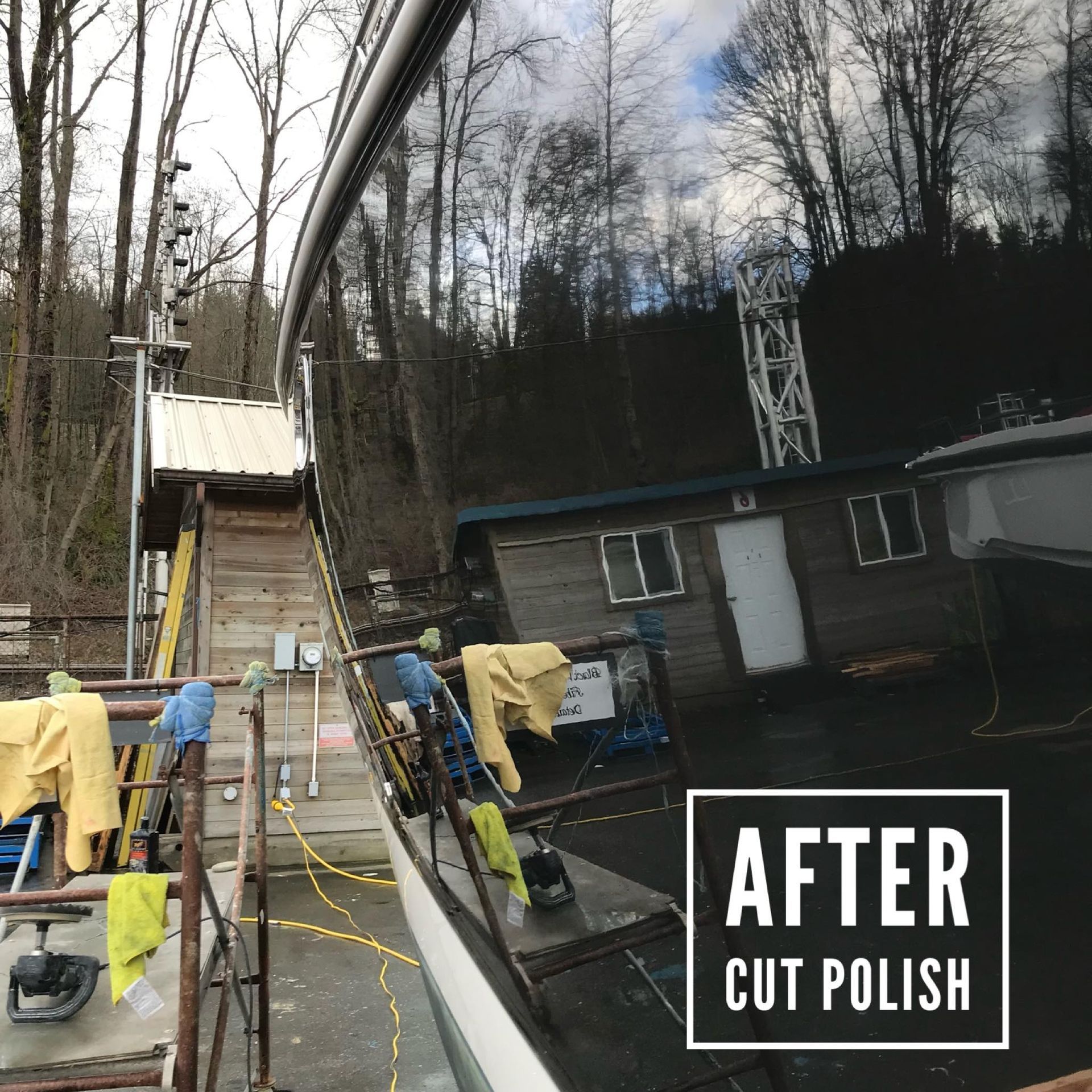 Shiny black boat hull after cut and polish, reflecting surrounding buildings and trees.