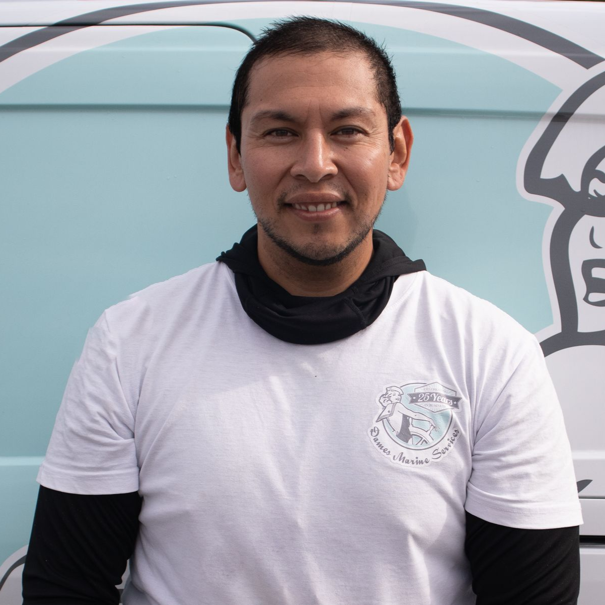 Man in white shirt with logo smiles in front of a light blue van.