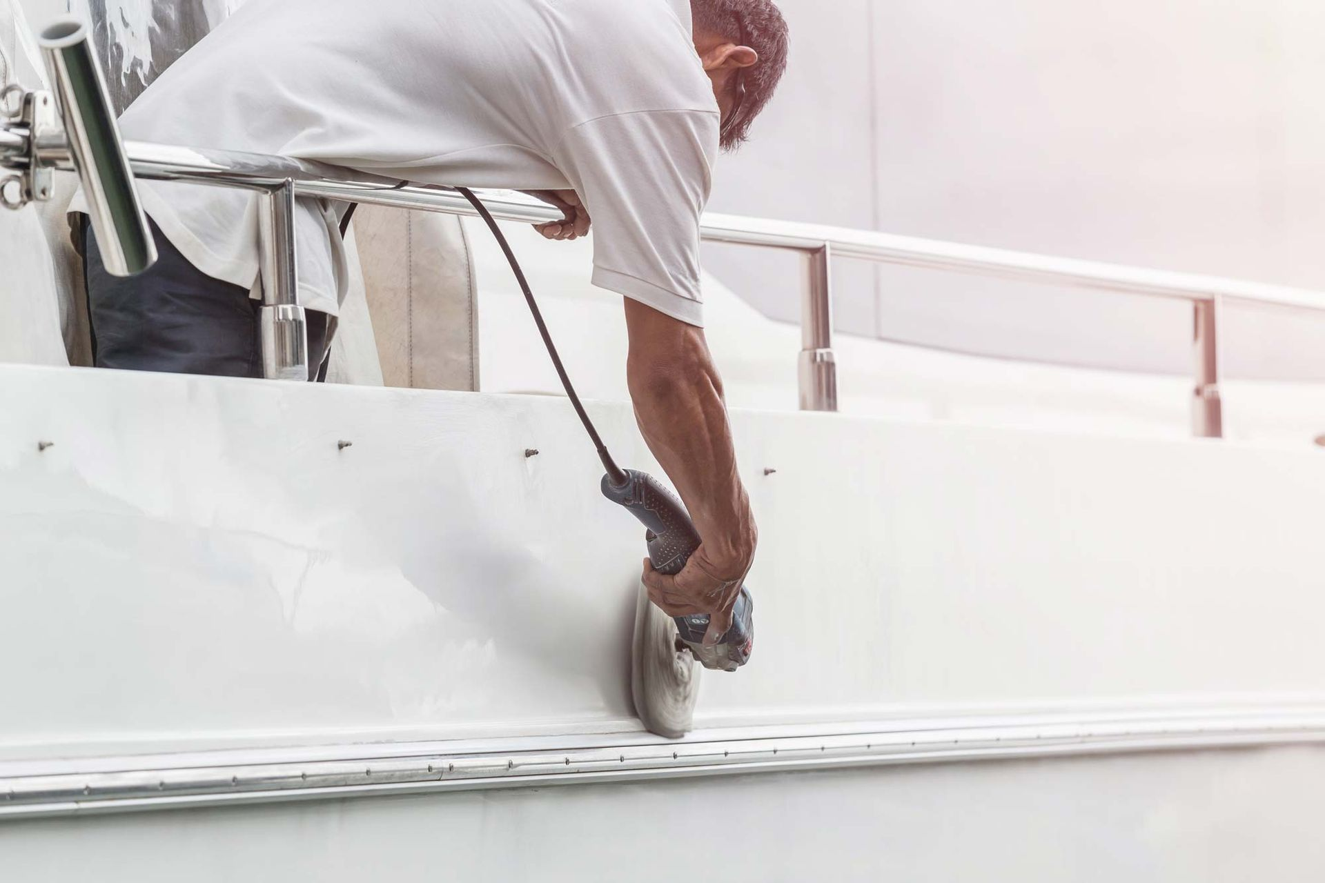 Person using a power tool to work on a white boat.