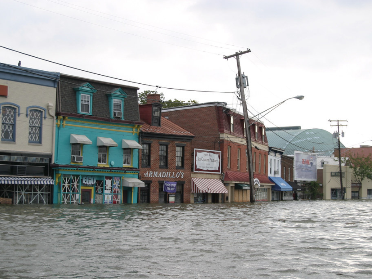 Buildings flooded by rising water in a street, overcast sky.