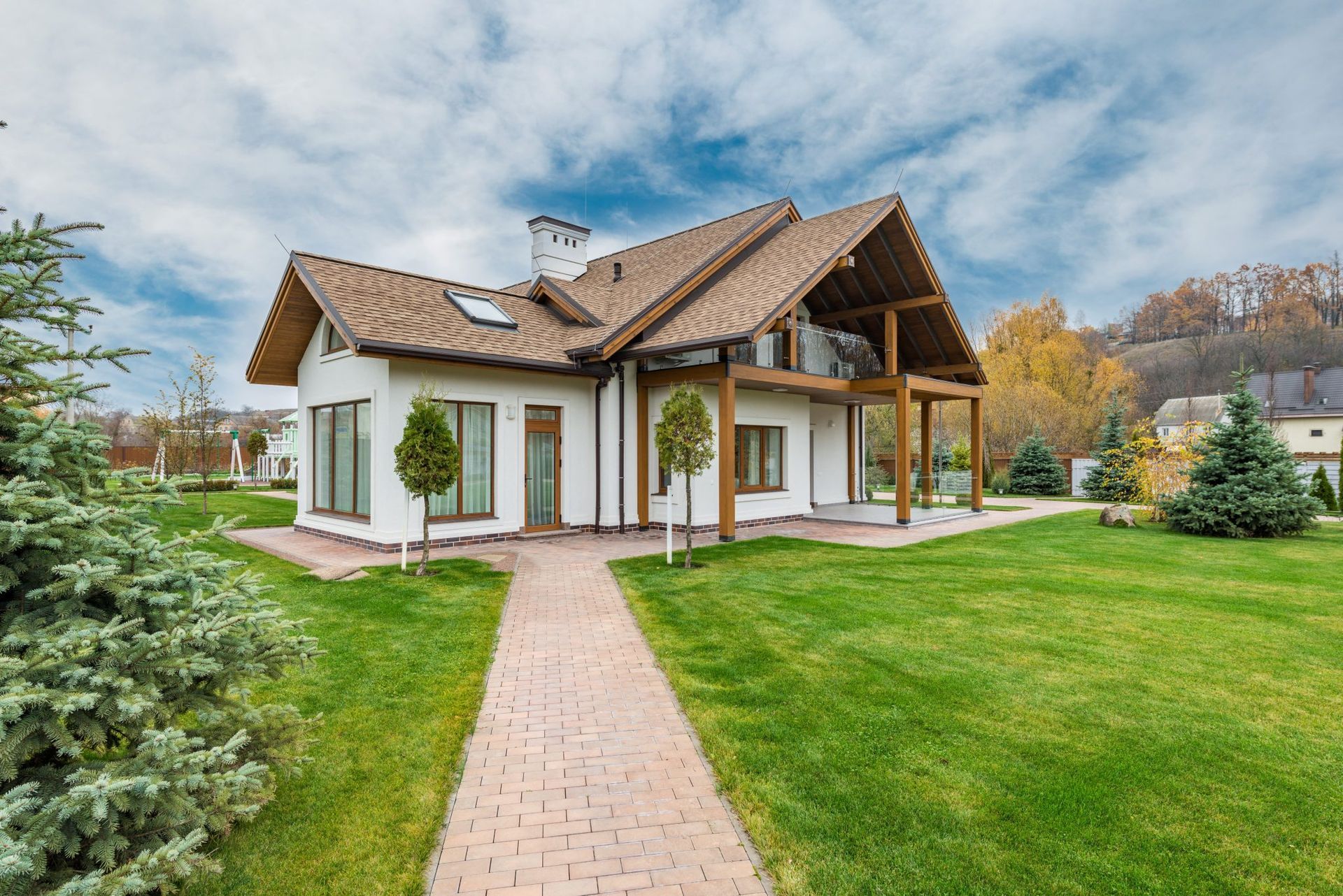 White house with brown roof and porch, on a green lawn, brick walkway, blue sky with clouds.
