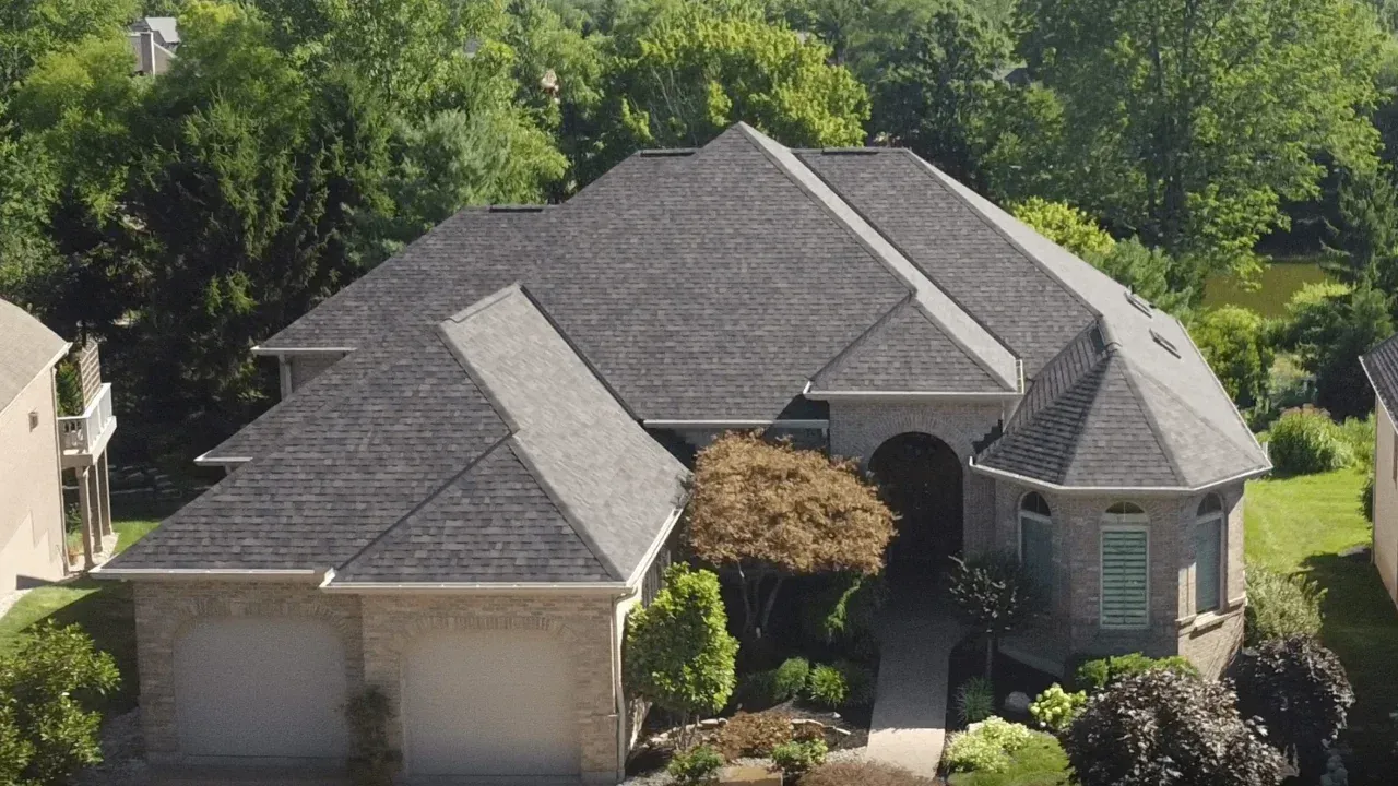 Gray-roofed brick house with a front lawn and a two-car garage, surrounded by trees.
