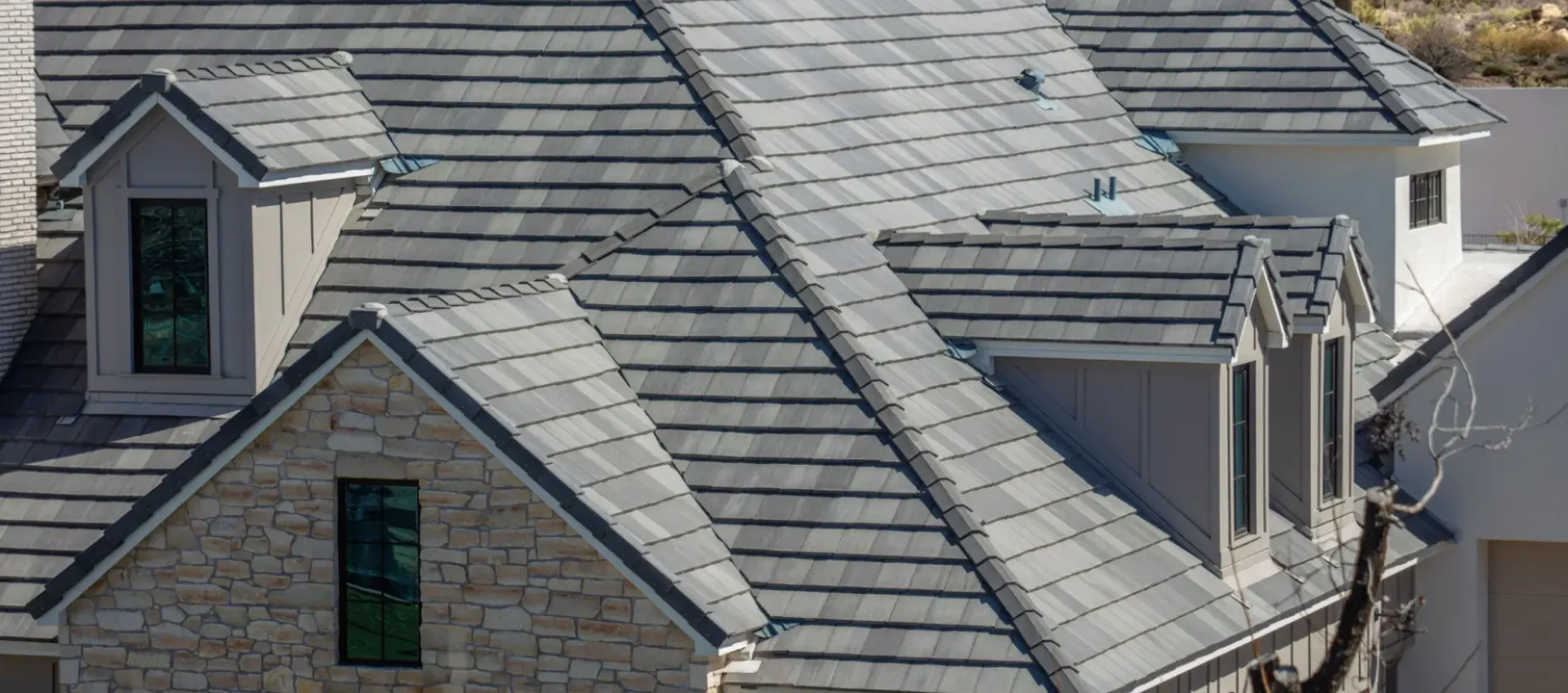 Gray shingled roof of a house with multiple dormers; sunny outdoor setting.