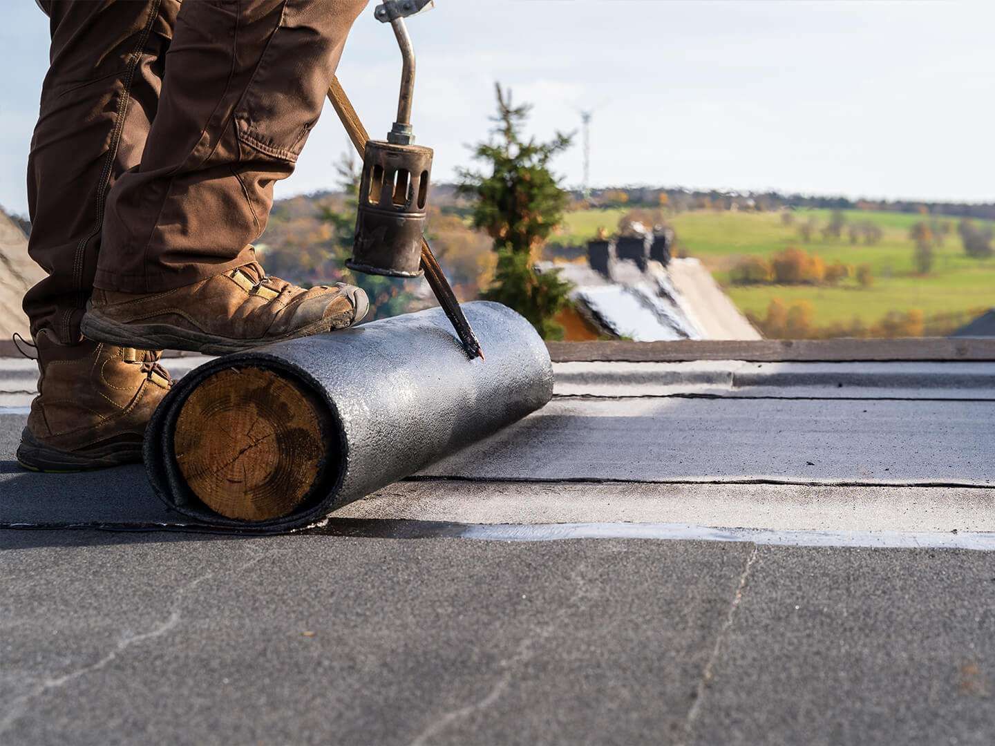 Roofer applying roofing material with a torch on a flat roof.
