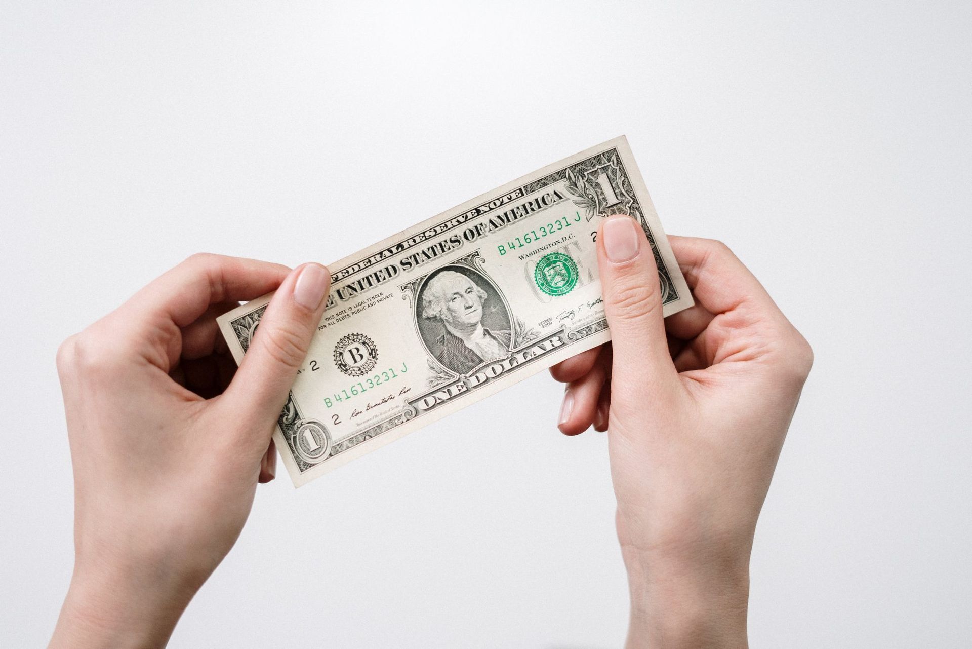 Close-up of a person's hands holding a one-dollar bill against a white background.