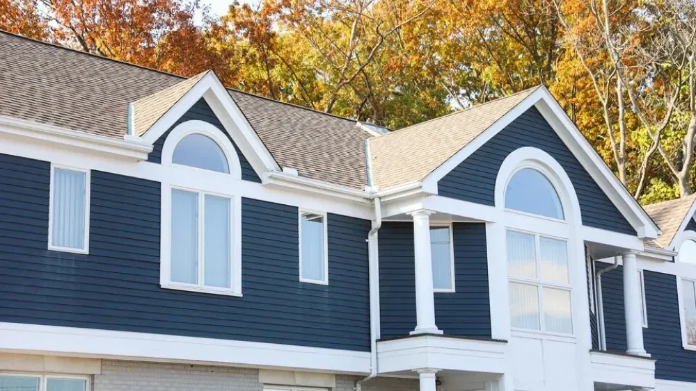 A blue house with arched windows and a white porch column, framed by colorful autumn trees