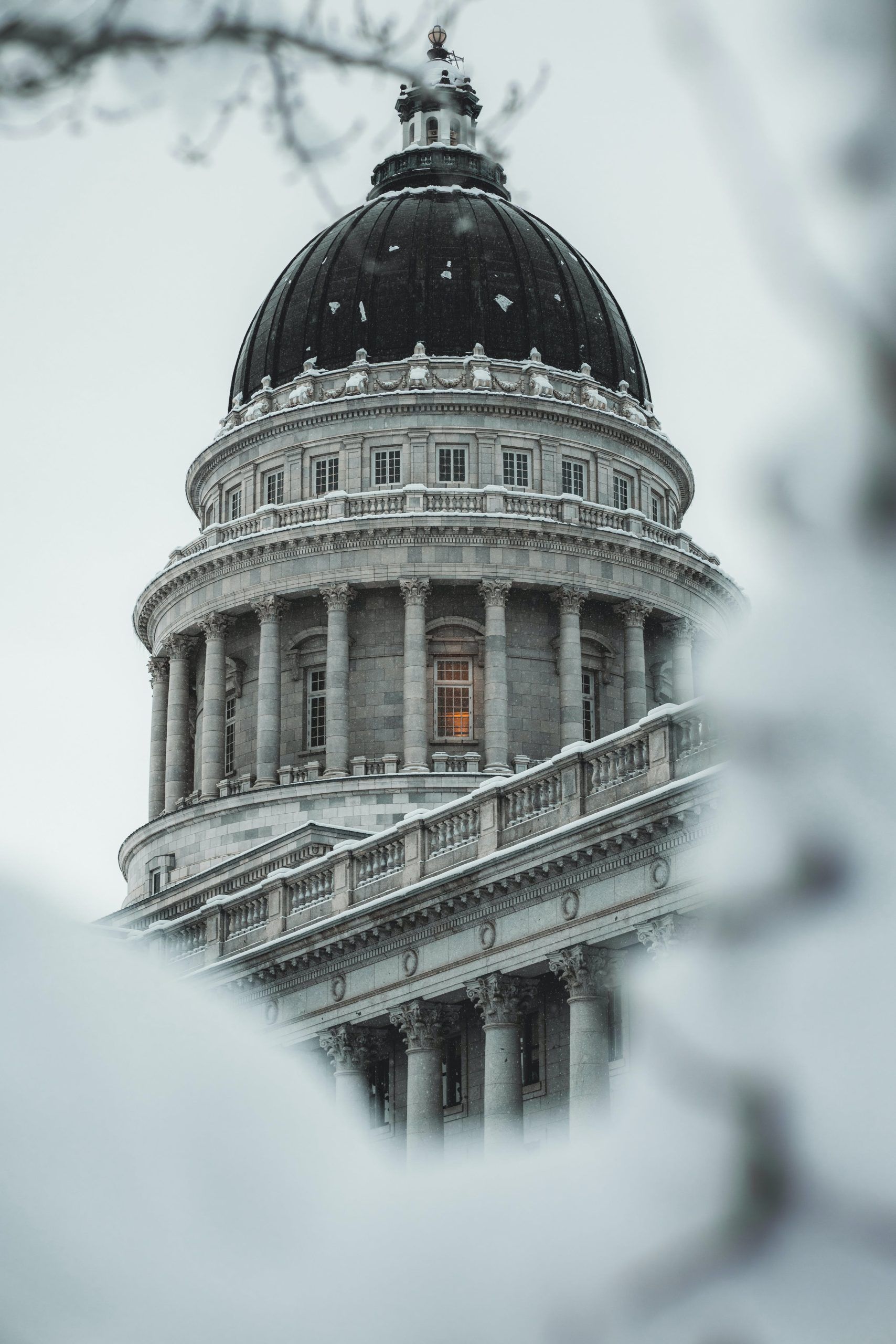 A large dark dome of a building featuring classical architecture and a light dusting of snow