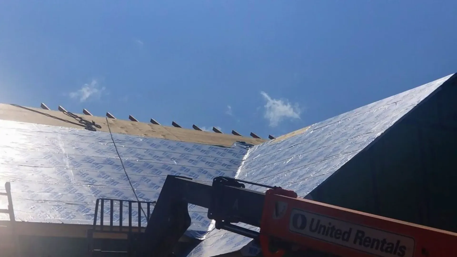 Roof under construction with protective underlayment and lift equipment nearby