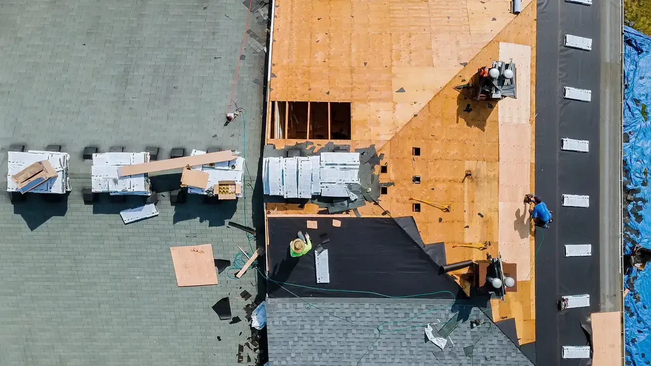 Roof being replaced; workers on wood and asphalt; equipment and materials are present.