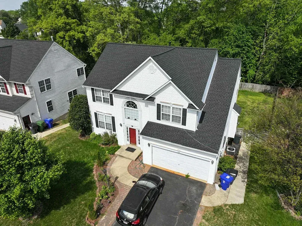 Asphalt shingle installed on a white residential home with black shutters in Maryland.