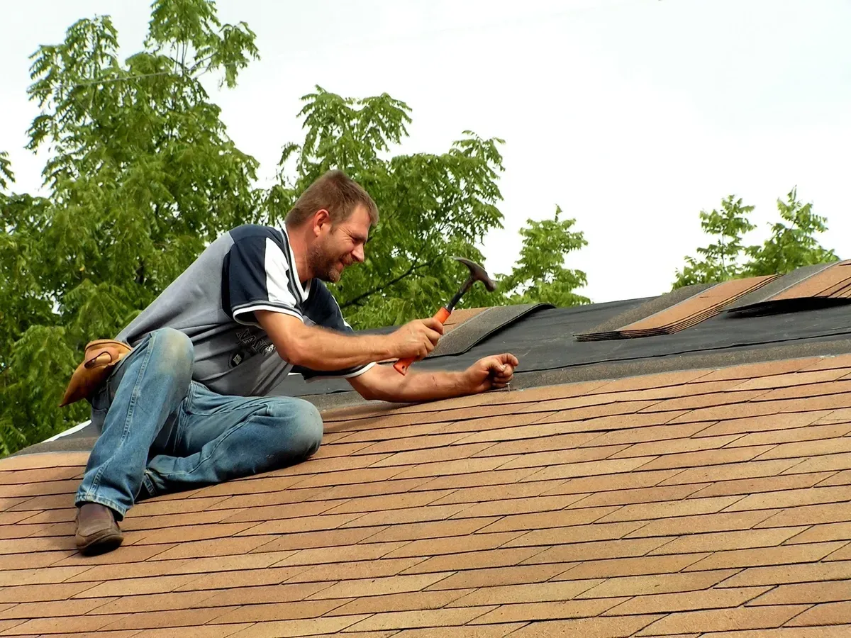 Man on roof hammering shingles.