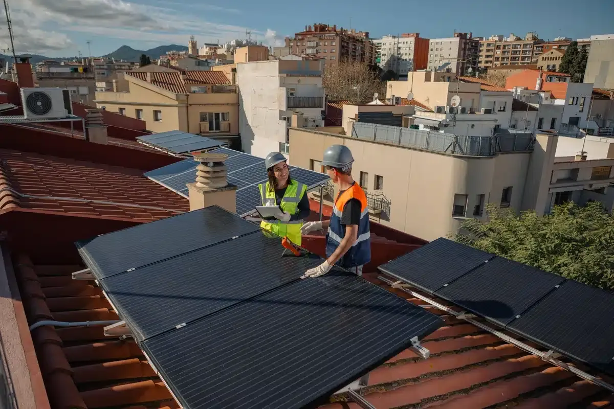 Two workers installing solar panels on a rooftop with a city backdrop.