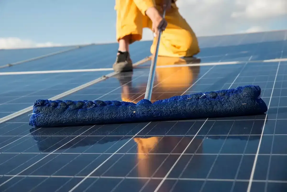 Person cleaning solar panels with a blue squeegee on a sunny day.