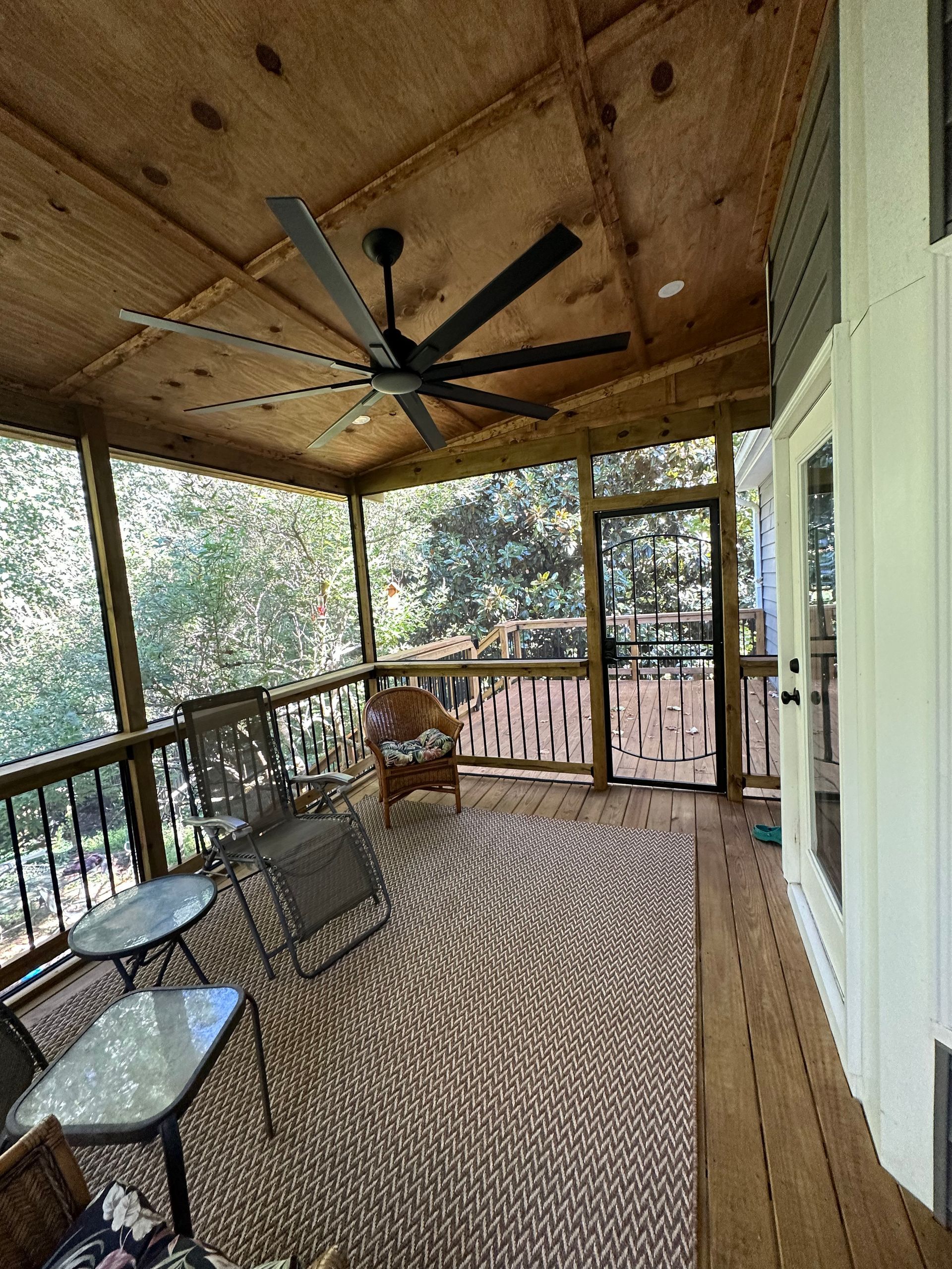 A screened in porch with a ceiling fan and chairs.